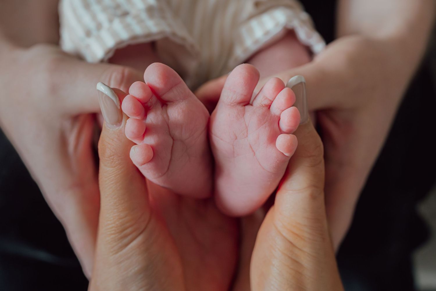 Close-up of newborn baby feet cradled gently in parents hands, showcasing tiny toes and delicate skin.