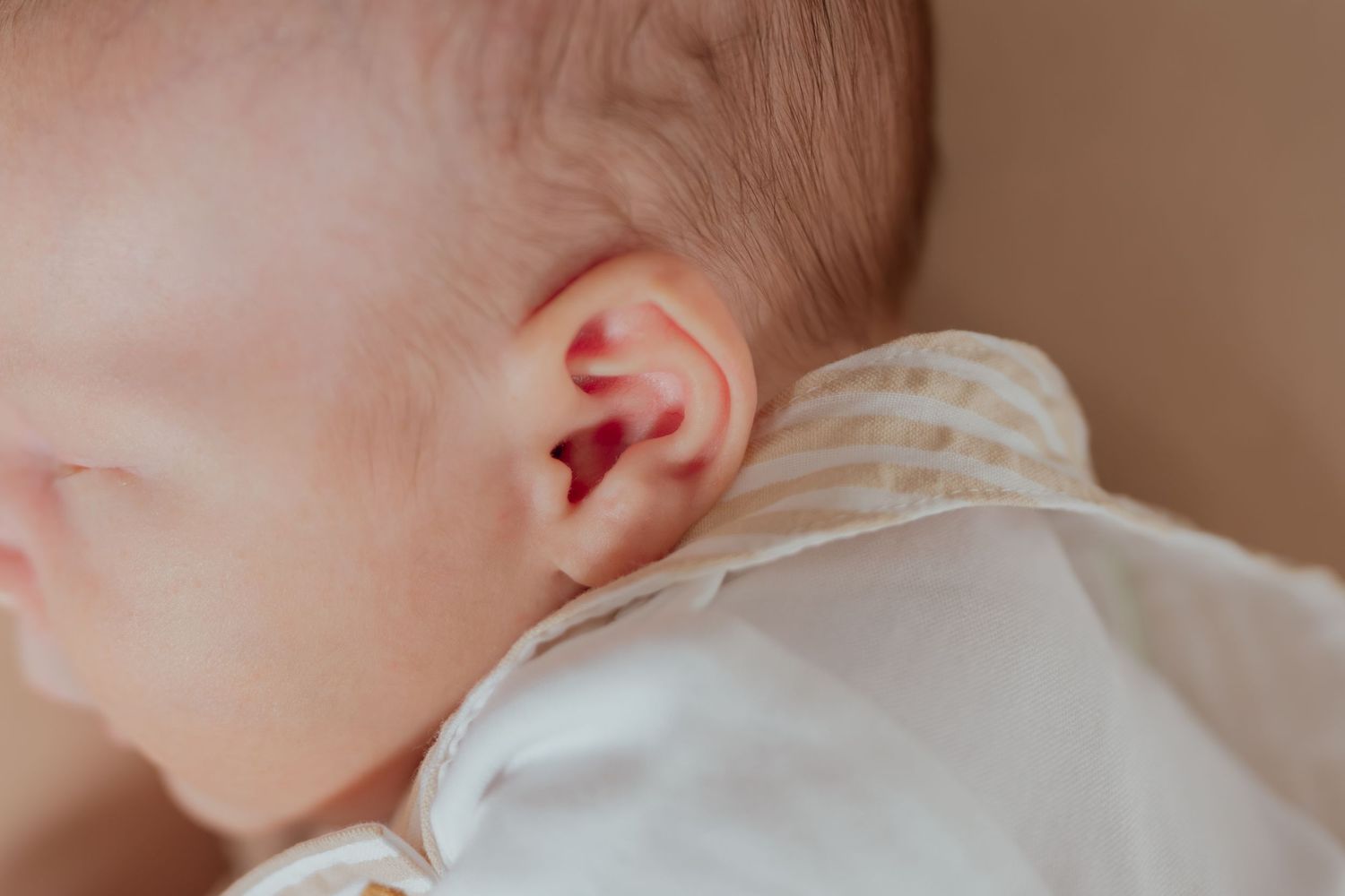 Close-up of a newborn baby's ear and soft skin, wearing a white and gold striped onesie.