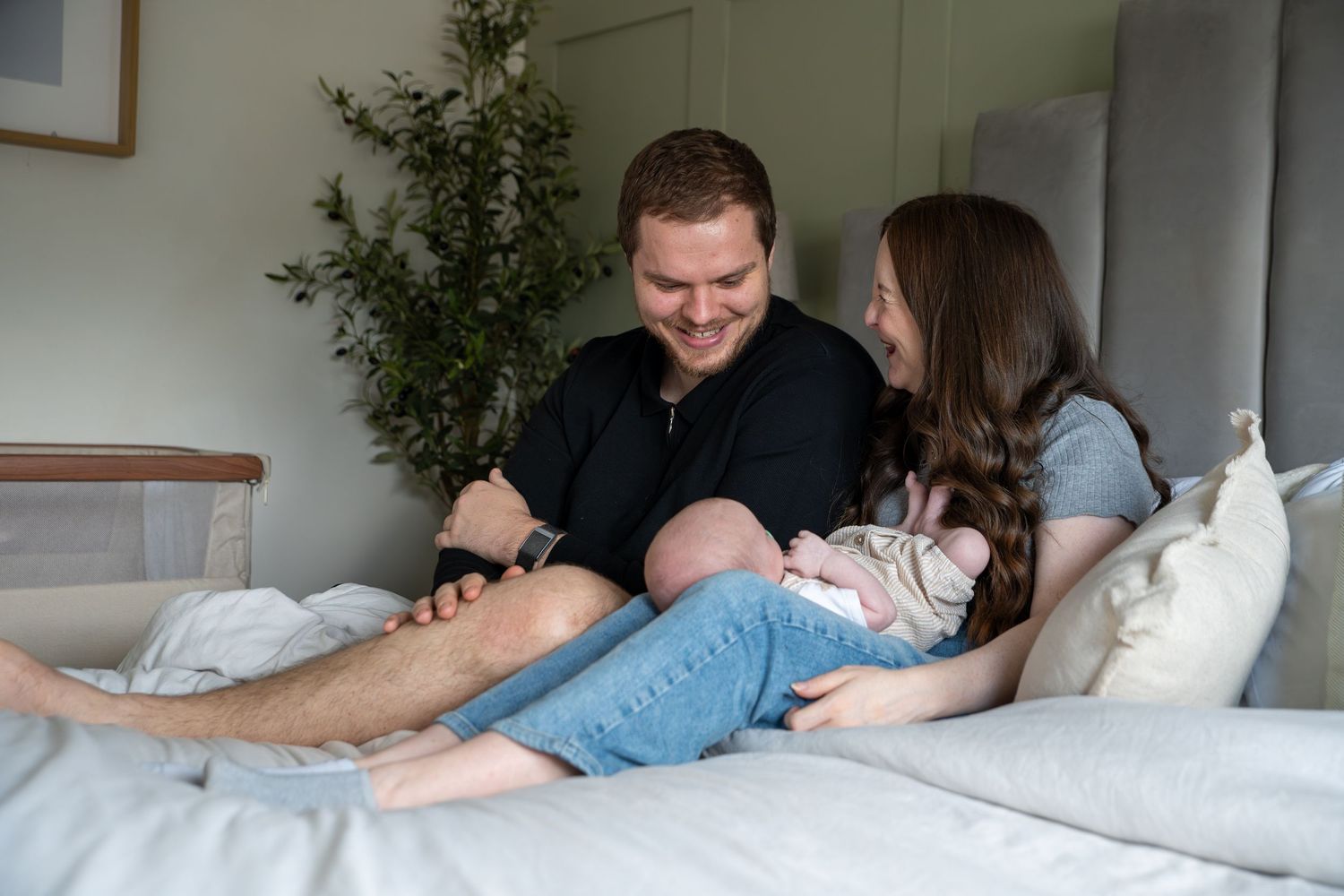 An intimate lifestyle family moment captured in a bright, minimalist bedroom setting.