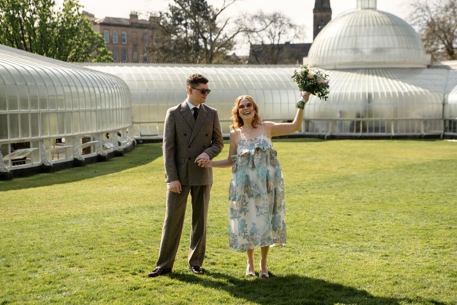 Couple walking along path near historic greenhouse structure.