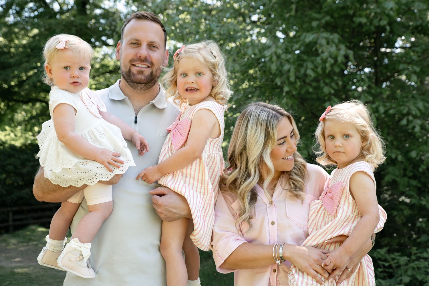 Family dressed in coordinating pink and white outfits poses outdoors in summer.