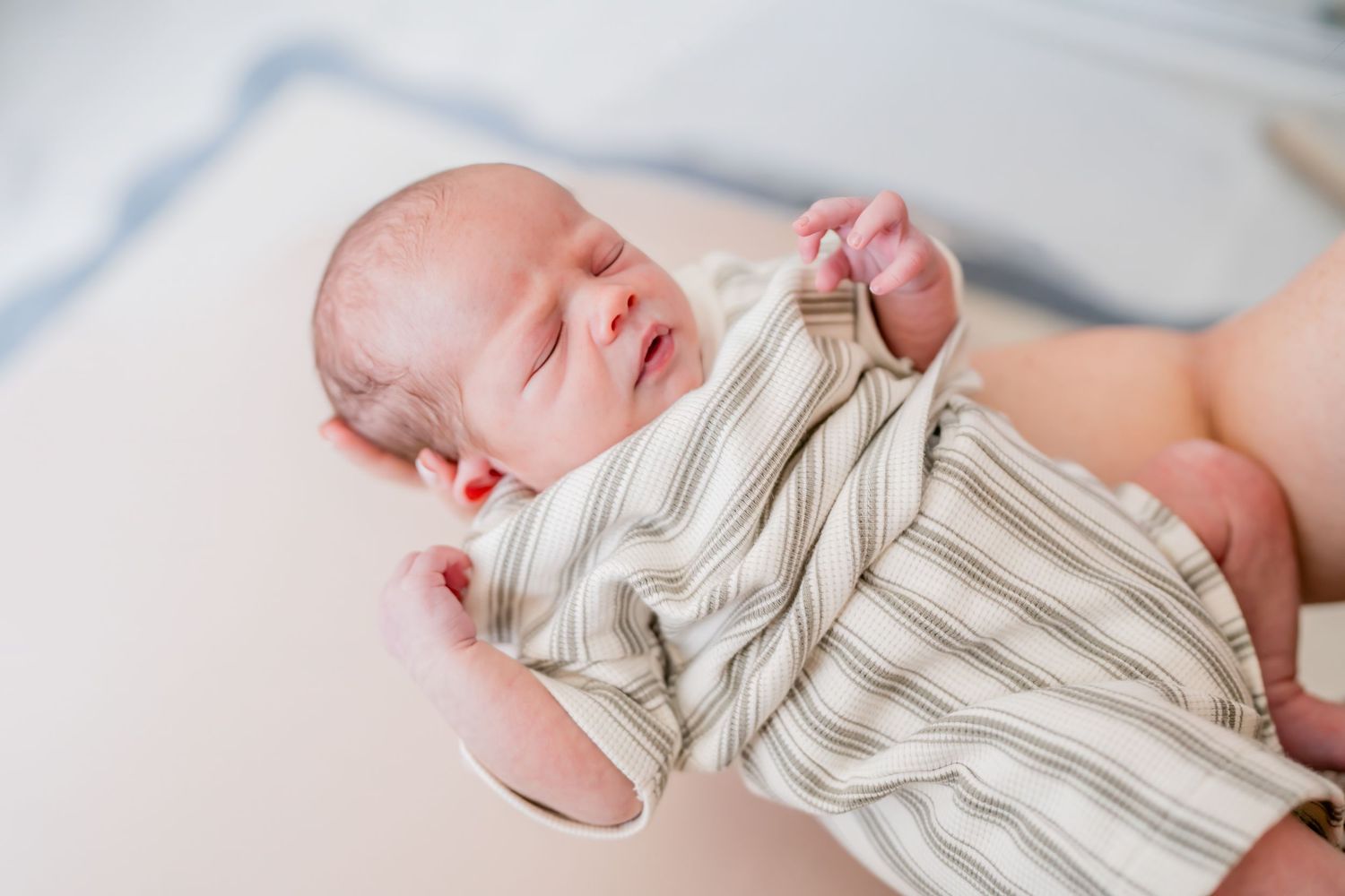 Peaceful newborn baby sleeping in striped onesie, cradled in adult hands on soft white surface.