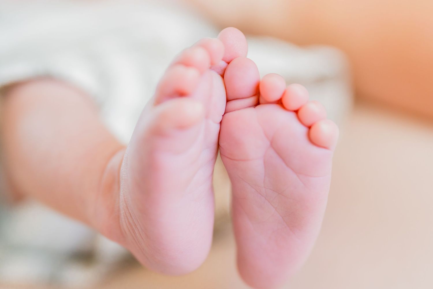 Close-up of adorable newborn baby feet with tiny toes resting on a soft blanket.