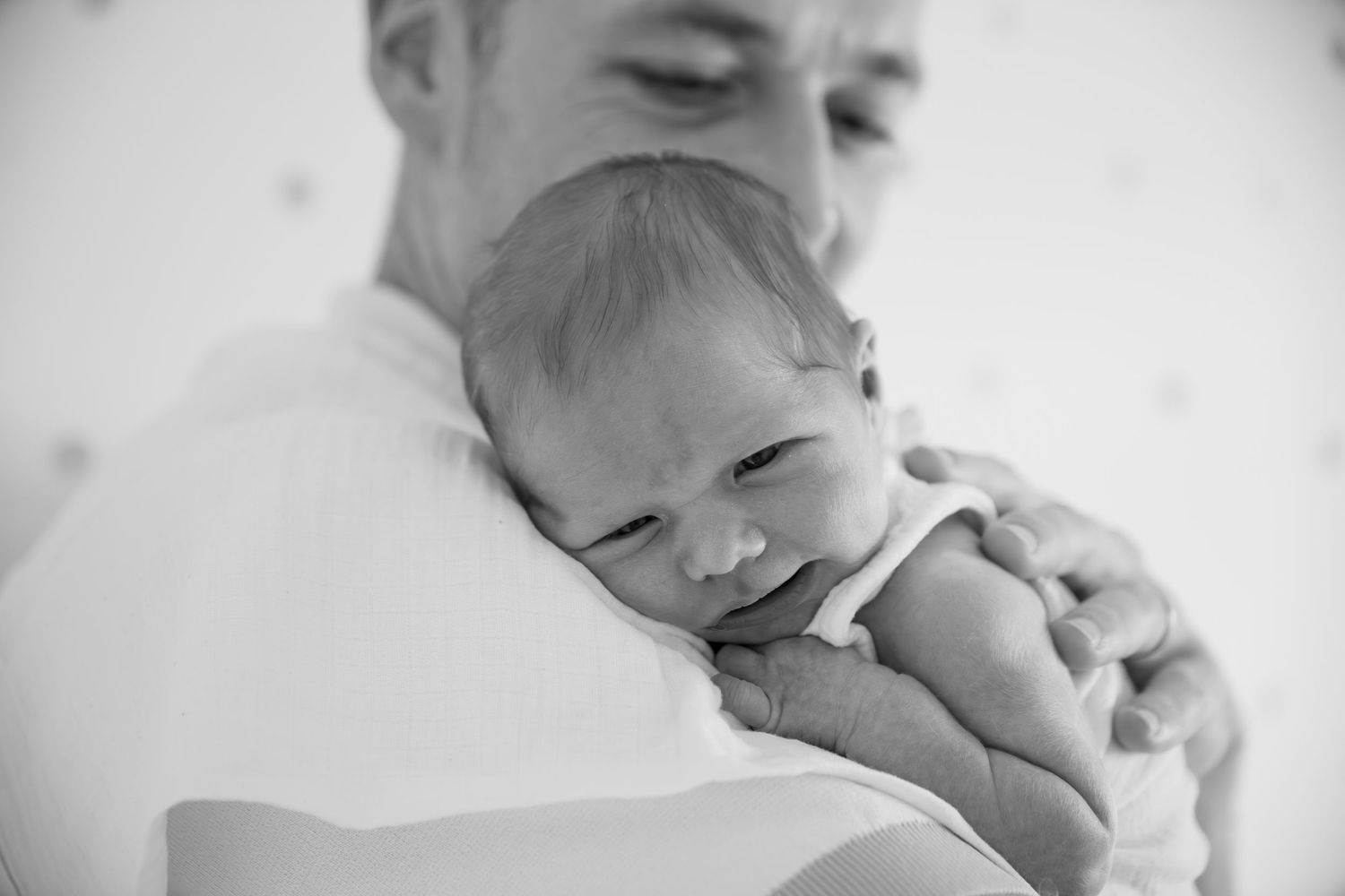 Tender black and white portrait of a sleeping newborn being cradled against a shoulder.