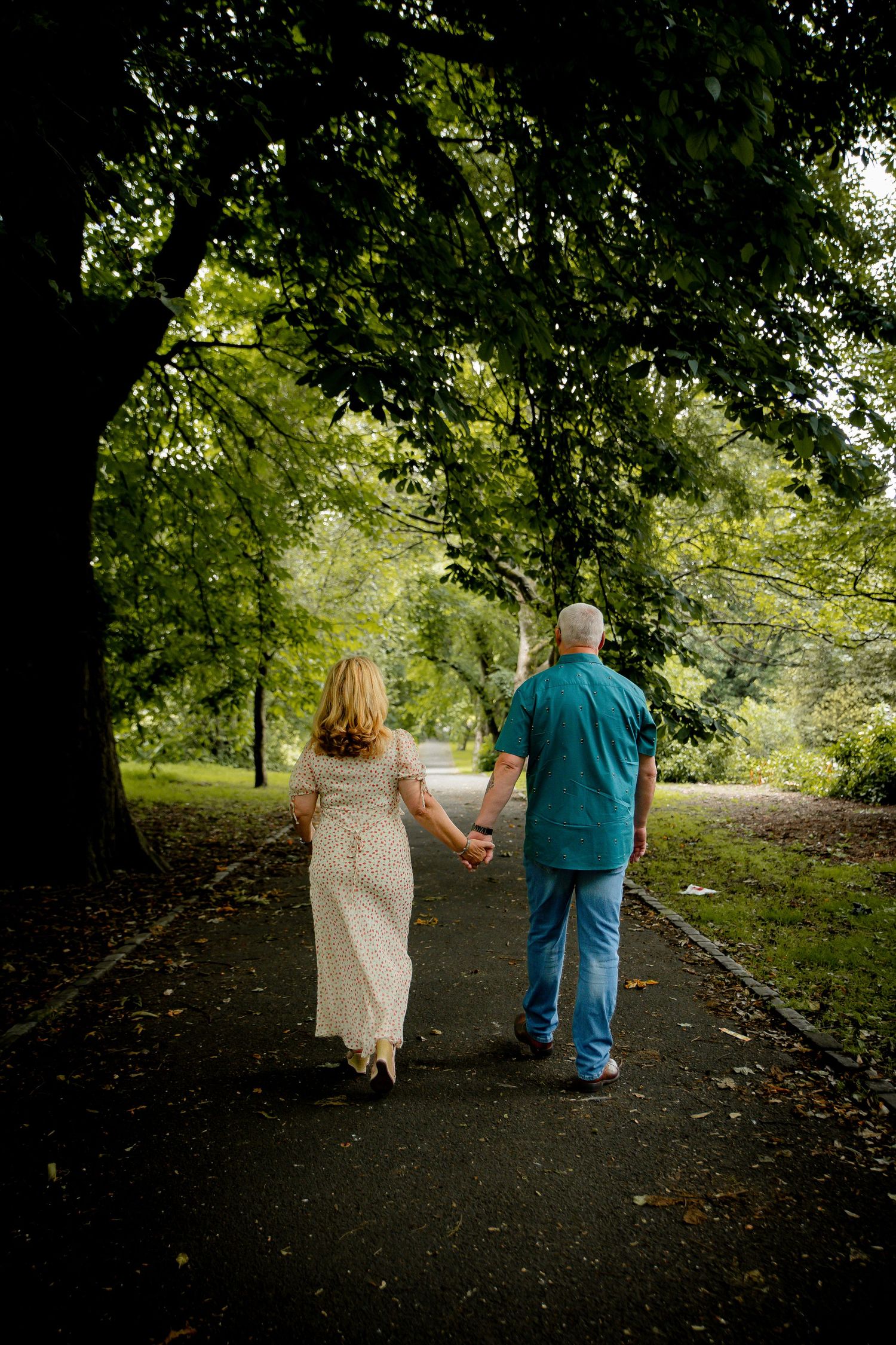 Couple walking hand in hand down tree-lined path.