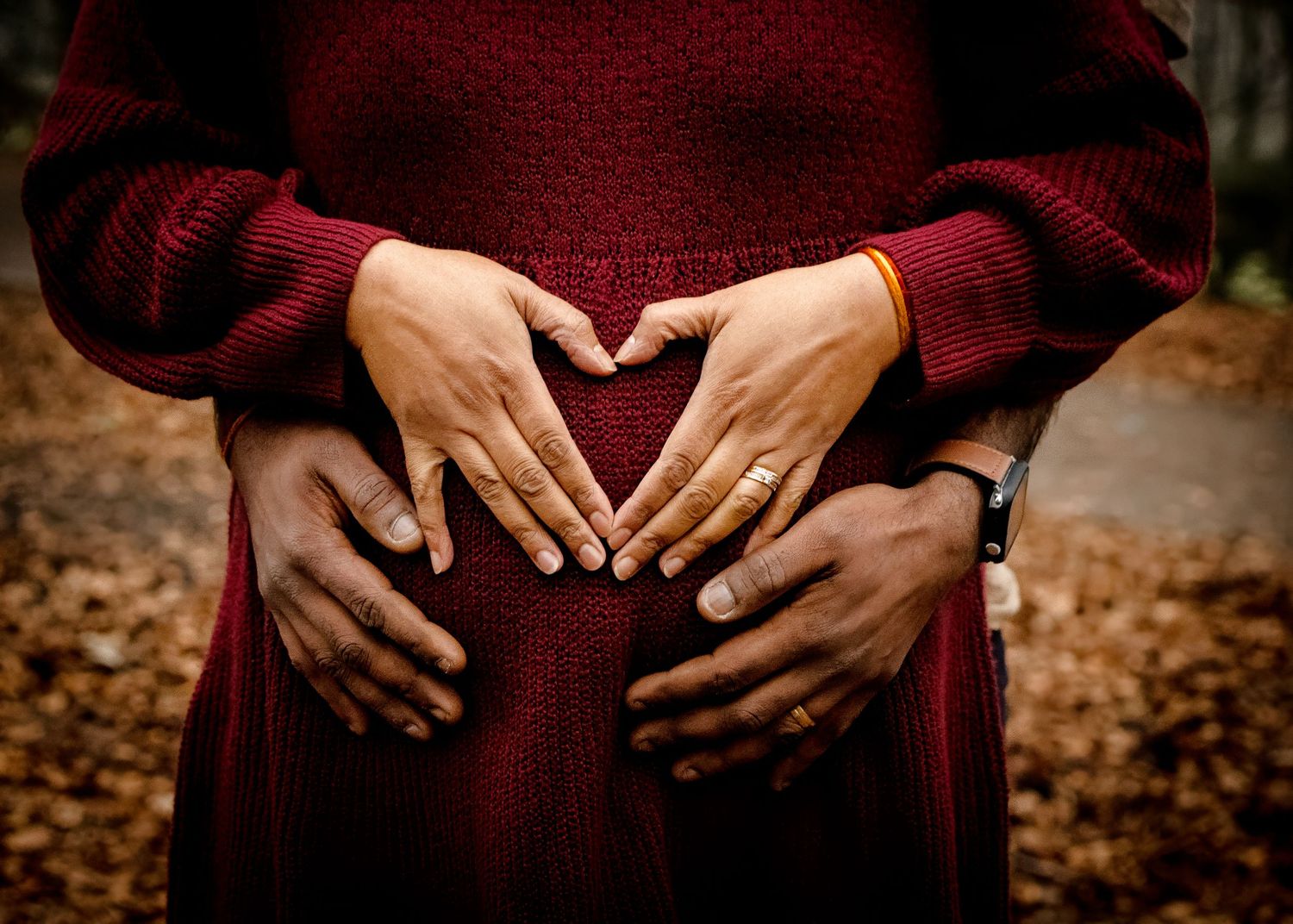 Close-up series of hands tenderly holding pregnant belly in burgundy sweater.