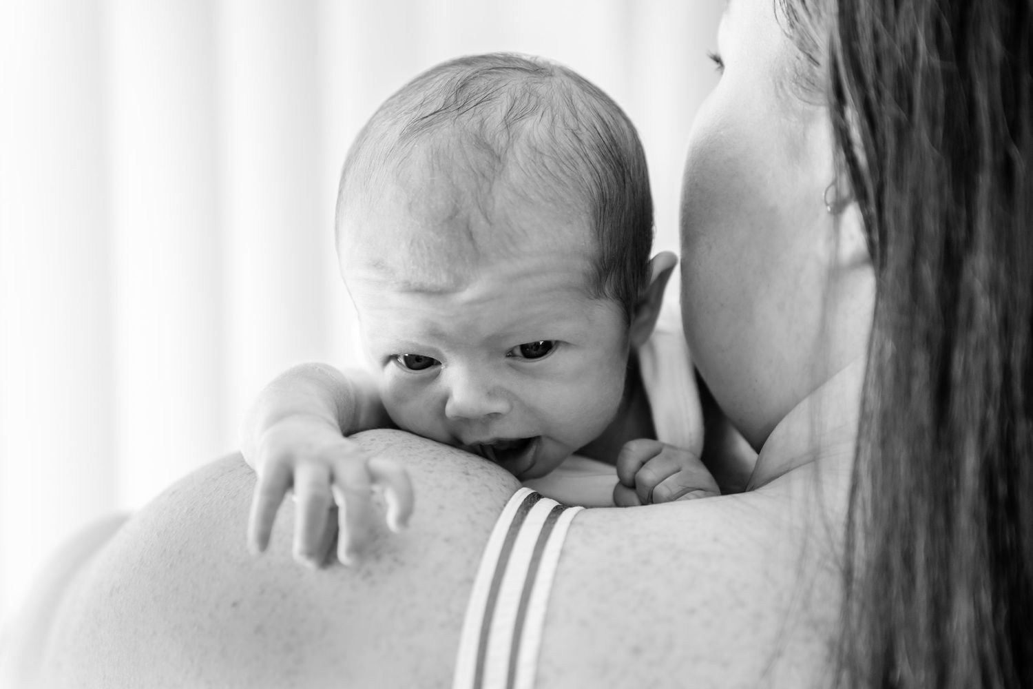 Black and white photo of a newborn baby resting on mother's shoulder with eyes open.