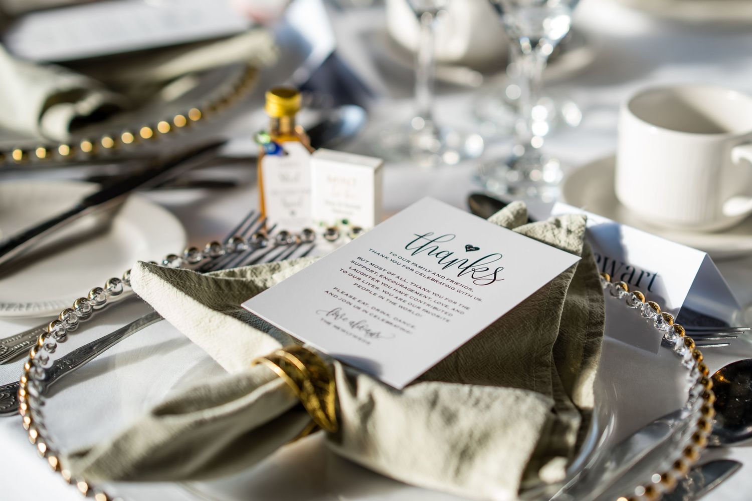 Elegant wedding table setting with beaded charger plate, folded napkin, and a thank you card among crystal glassware.