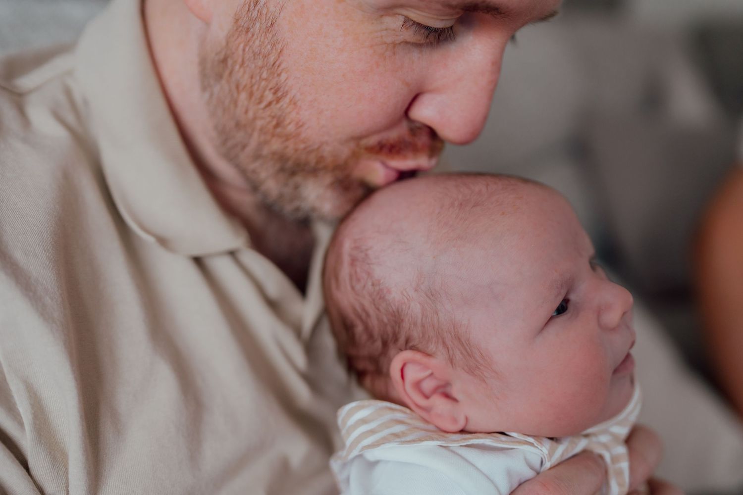 A bearded father gently kisses his newborn baby on the head, sharing a tender moment of love and bonding.