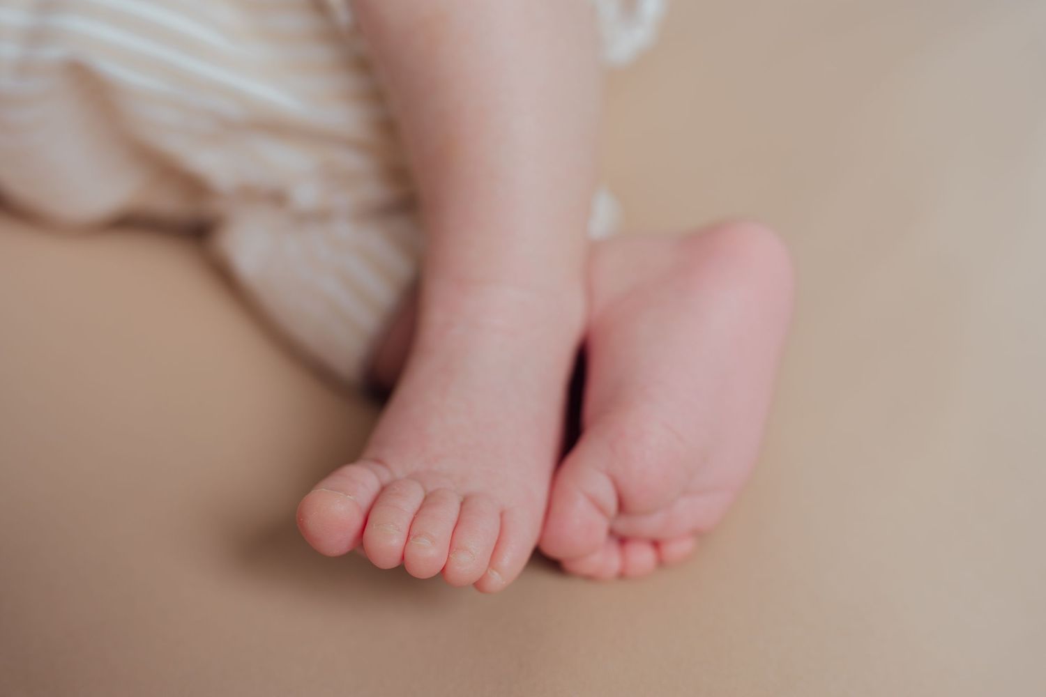 Close-up of adorable newborn baby feet resting on a soft beige surface with a striped blanket in the background.