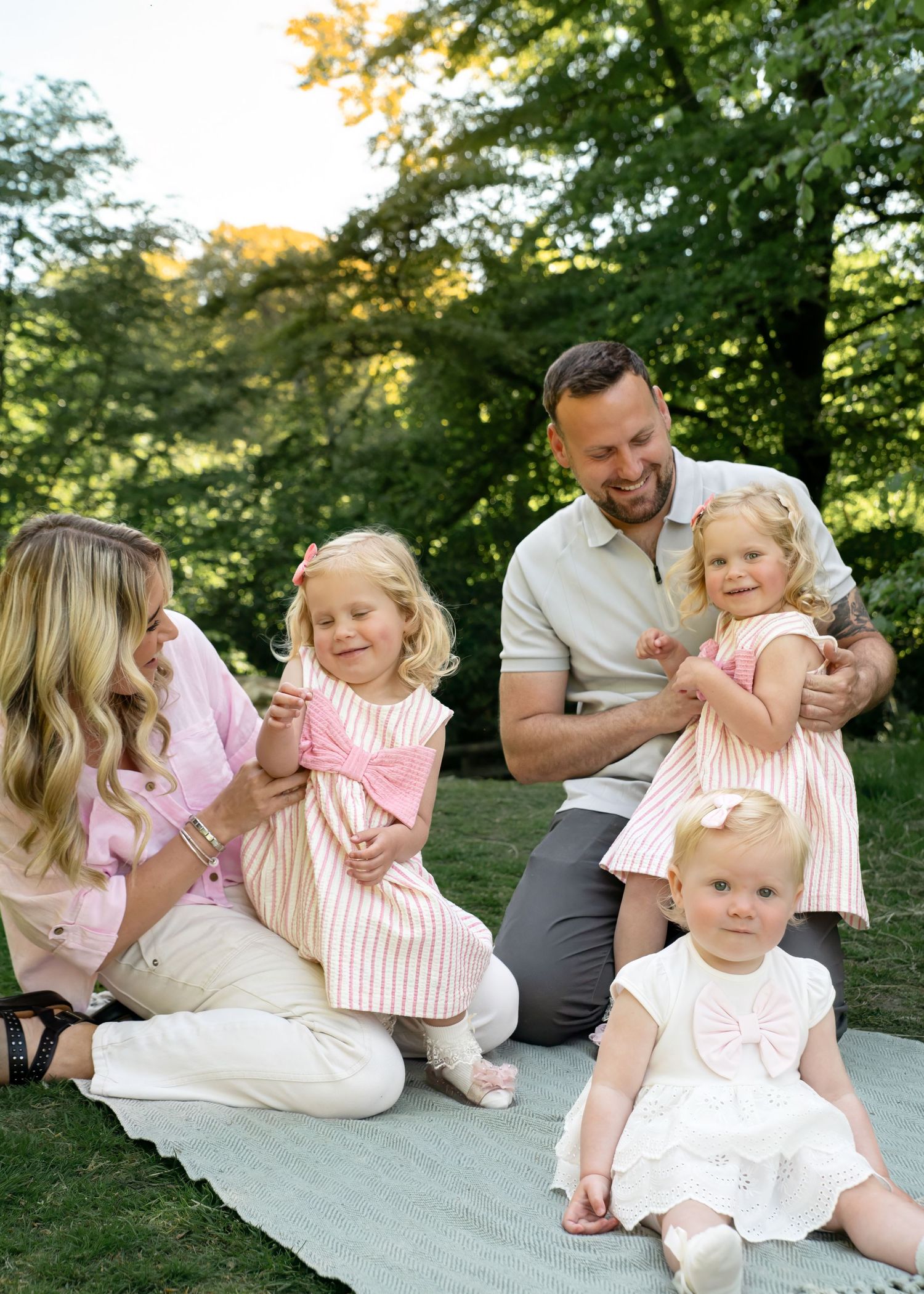 Family relaxing together on a white blanket in a park setting.