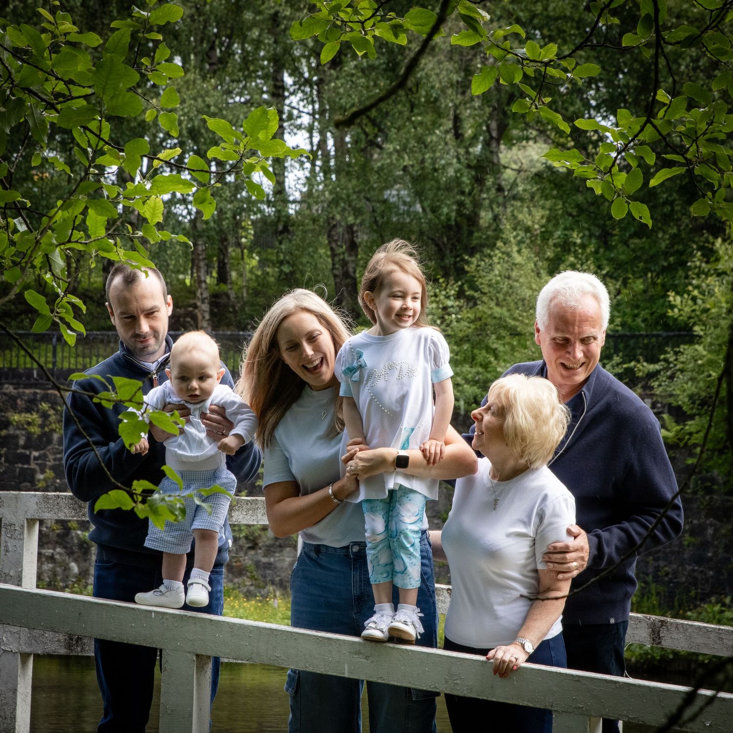 Family members gather together on a wooden bridge surrounded by green foliage.