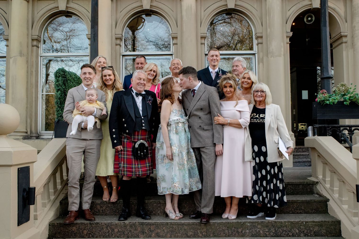 Wedding party poses together on grand stone staircase in formal attire.