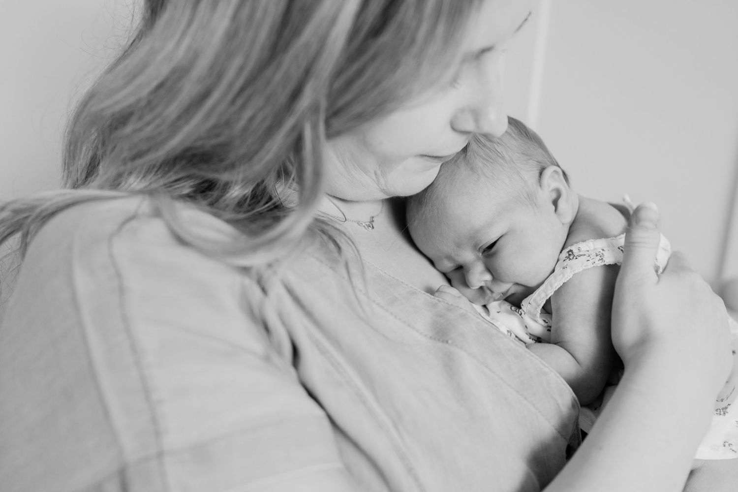 Black and white photo of a mother tenderly kissing her sleeping newborn baby held close to her chest.