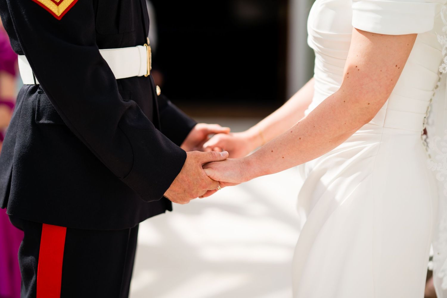 Military groom and bride in white dress holding hands at wedding ceremony.