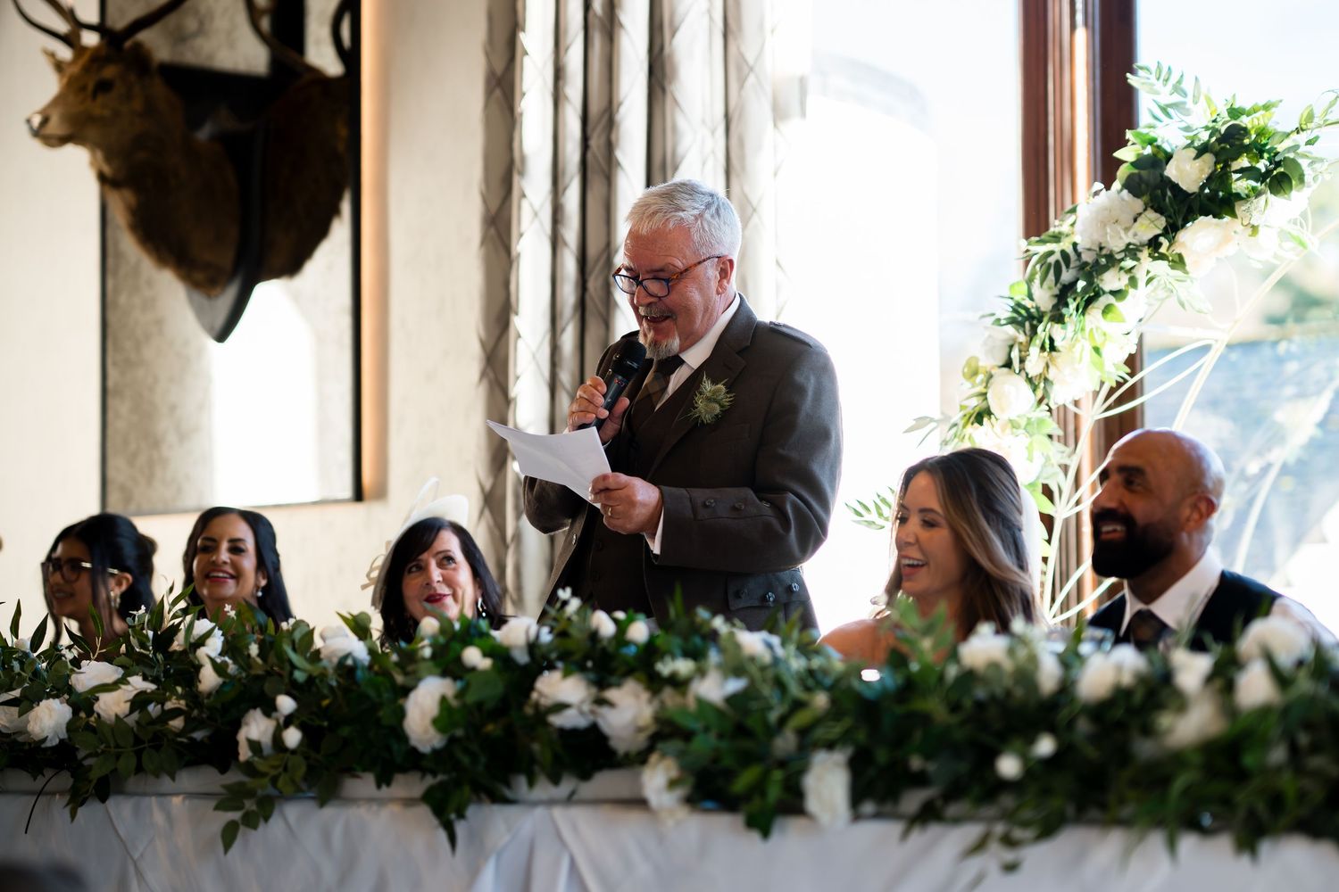 A group of people seated at a long banquet table decorated with white floral arrangements and greenery.