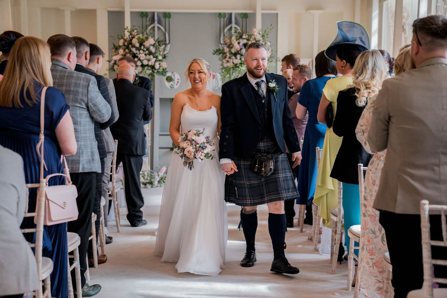 Bride and groom walk down the aisle at an elegant wedding ceremony, groom wearing a traditional Scottish kilt.