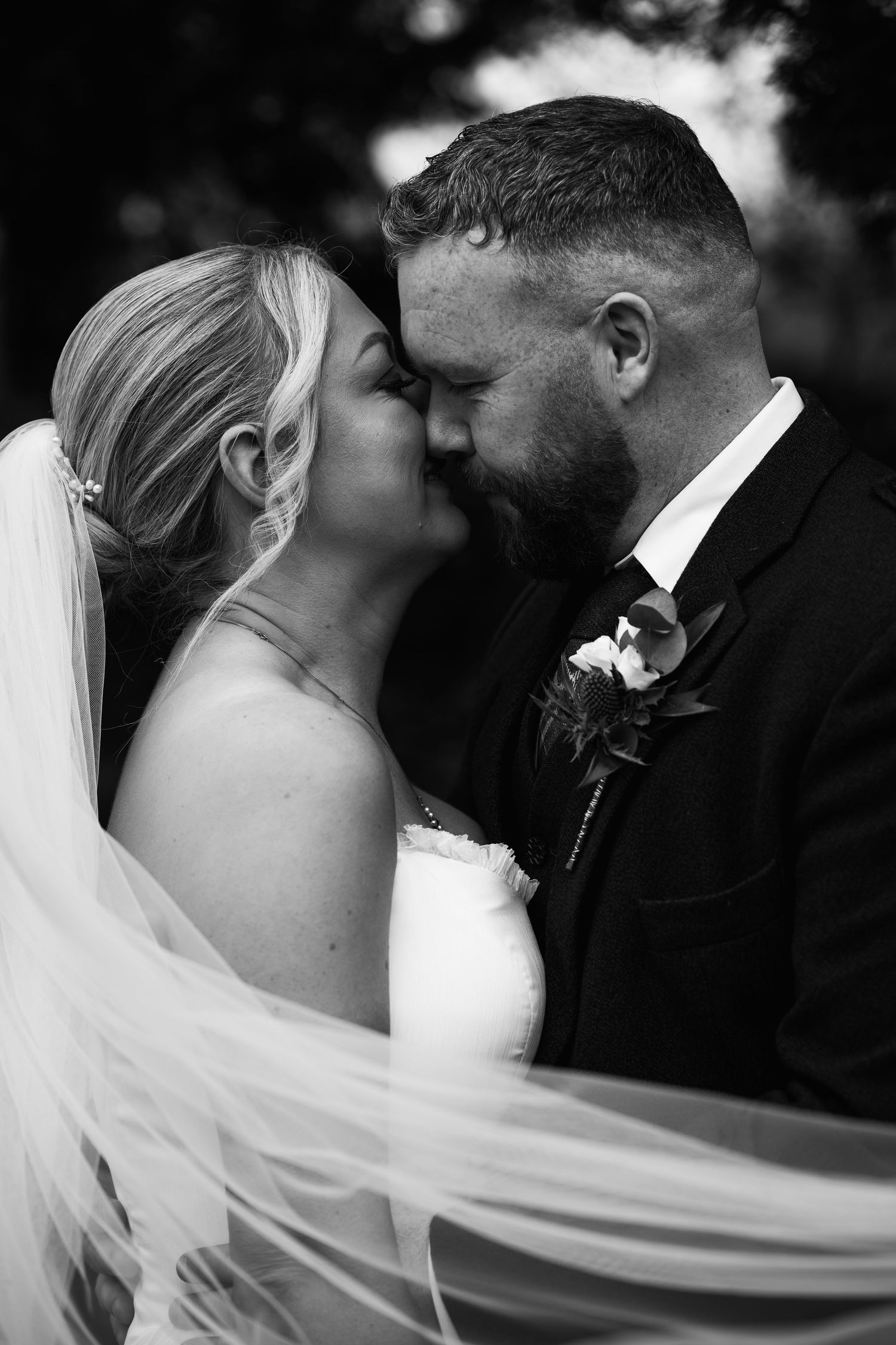 Black and white photo of a bride and groom sharing a romantic kiss, with her veil flowing in the breeze.