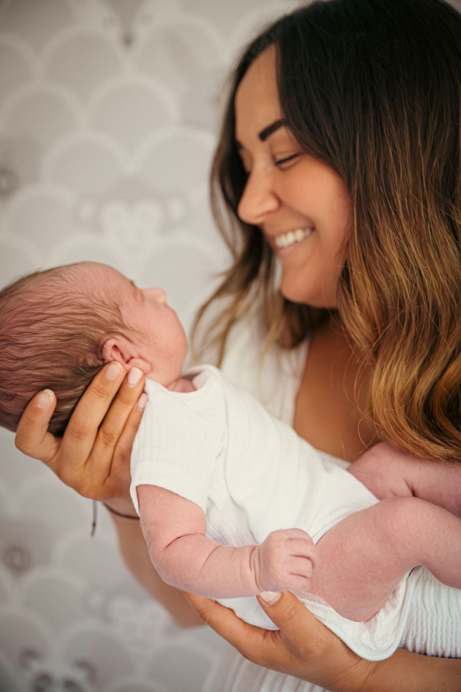 Smiling young mother gently cradling her sleeping newborn baby in her arms against a soft gray backdrop.