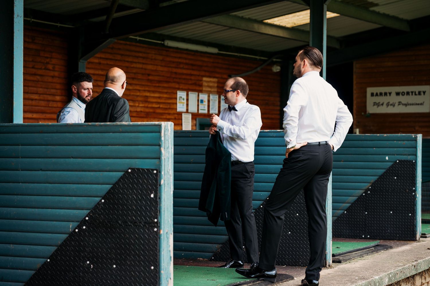 Men in formal attire socializing outside a clubhouse venue, preparing for a wedding or formal event.