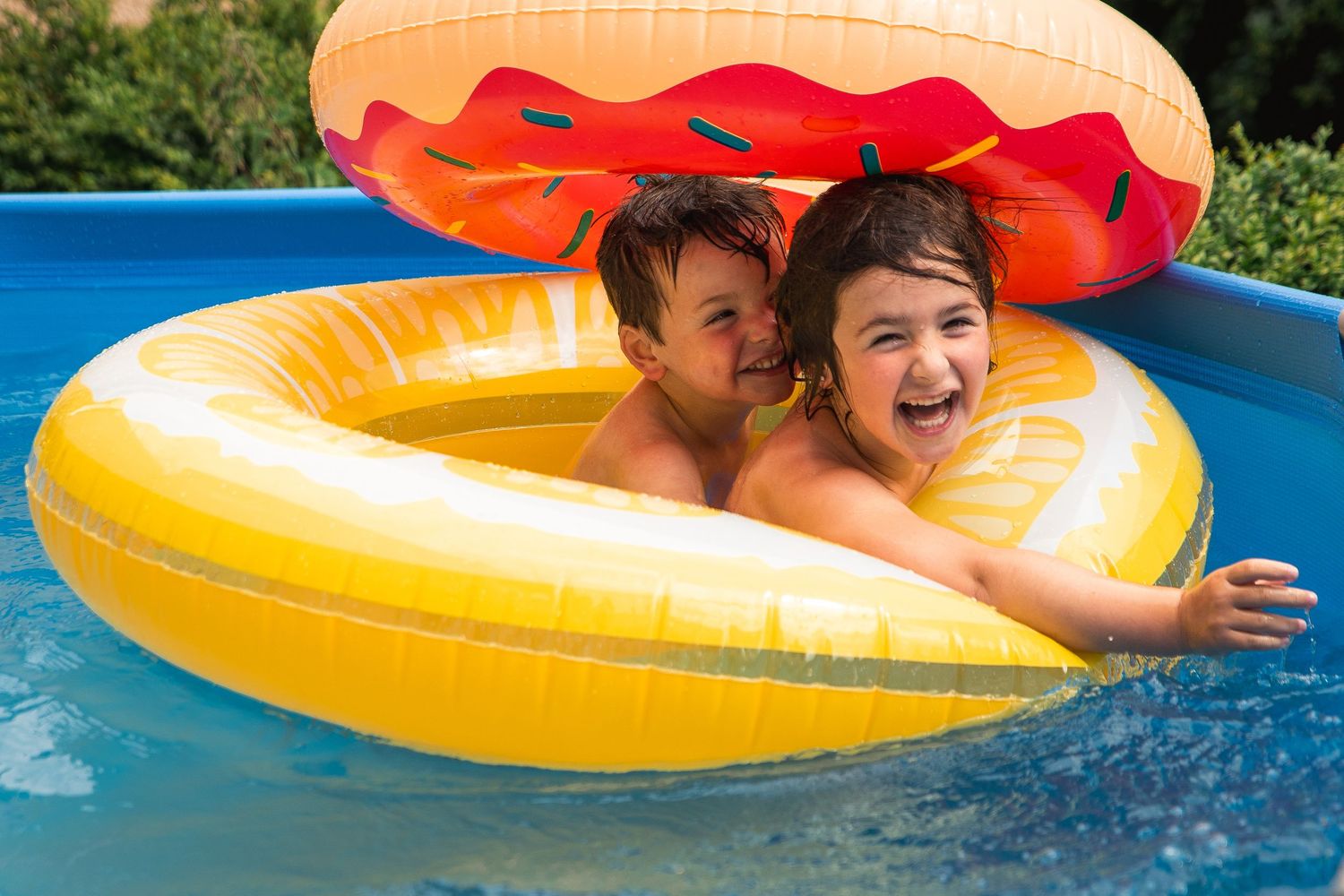 Two happy children laughing and splashing in a yellow lemon pool float on a sunny day.