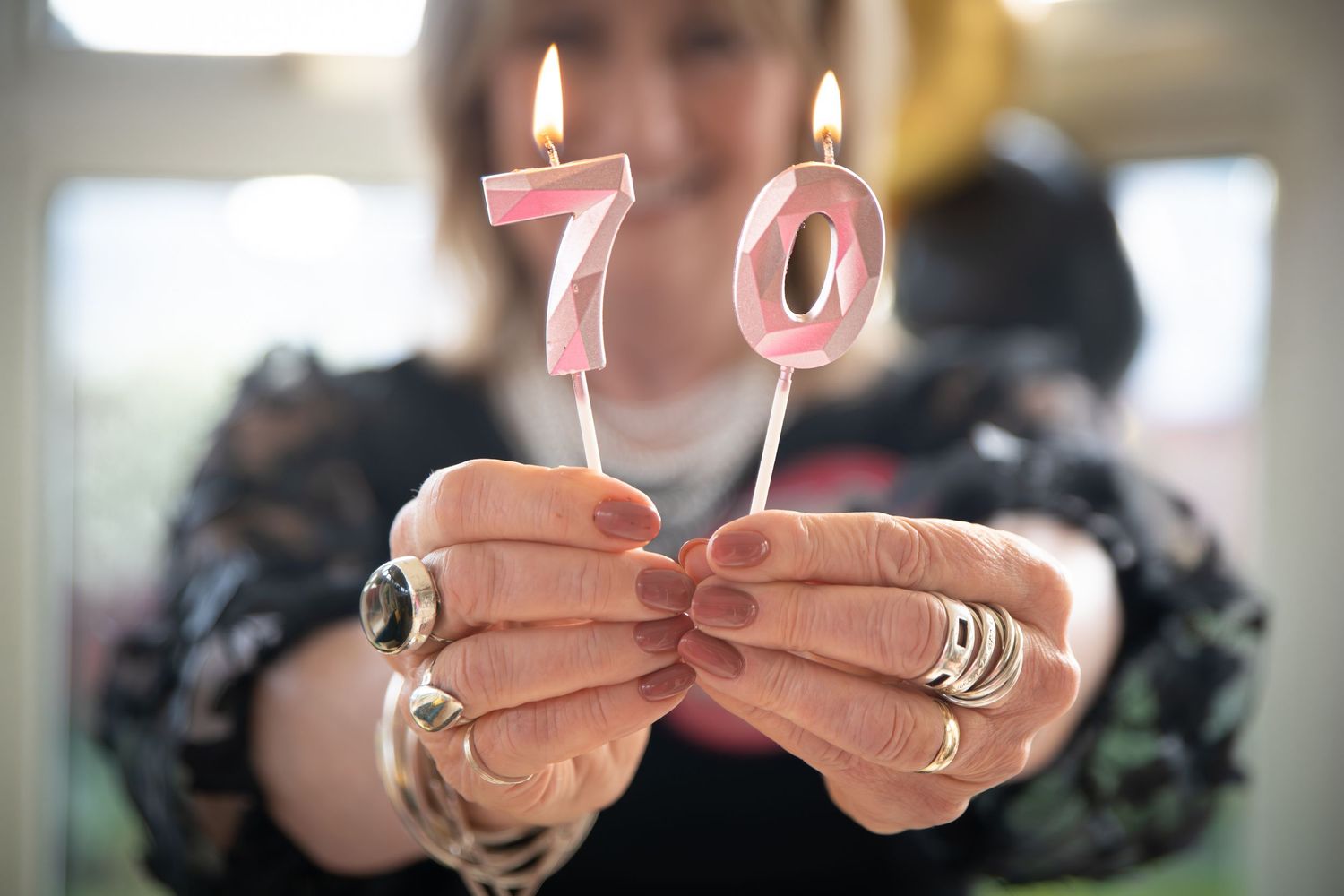 Woman holding two lit pink number 70 birthday candles, celebrating a 70th birthday milestone.