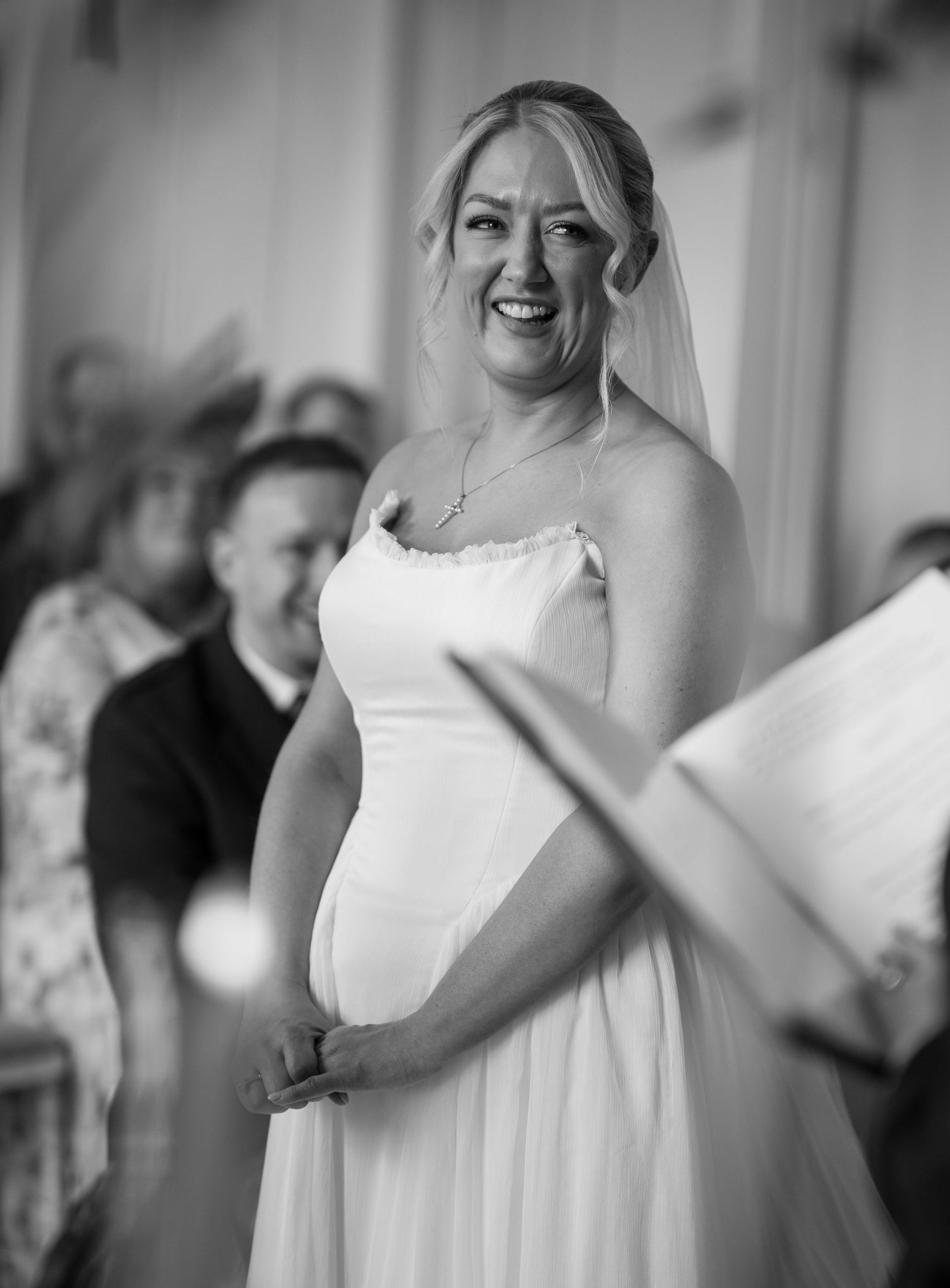 Black and white photo of a smiling bride in a wedding dress and veil during her ceremony.