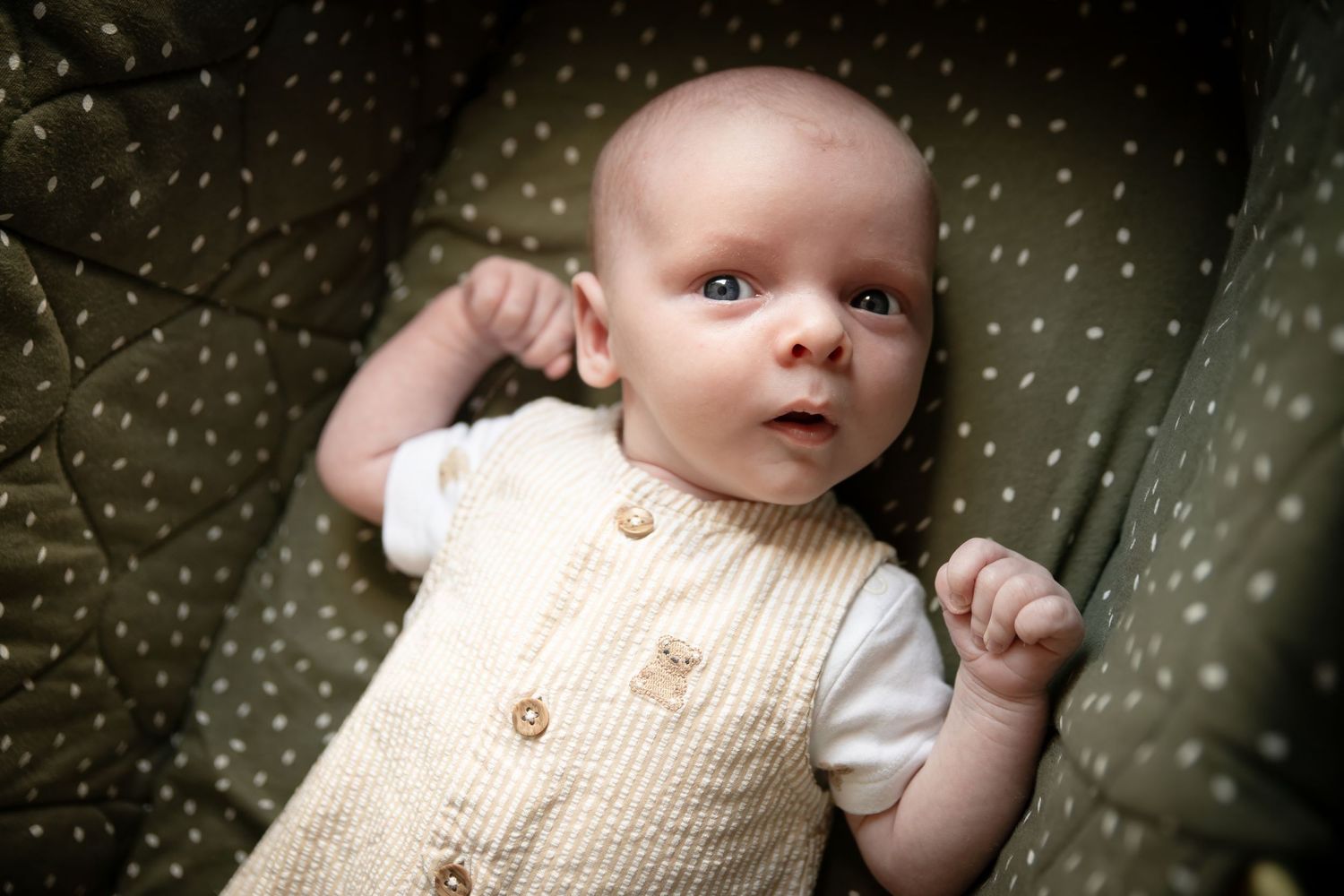 Baby in cream knit vest looking up with surprised expression.