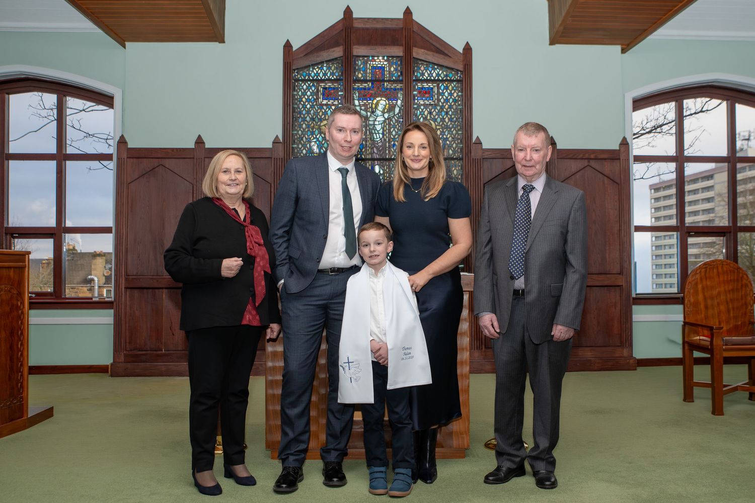 Family of five posing together in a church during a child baptism ceremony wearing formal attire.