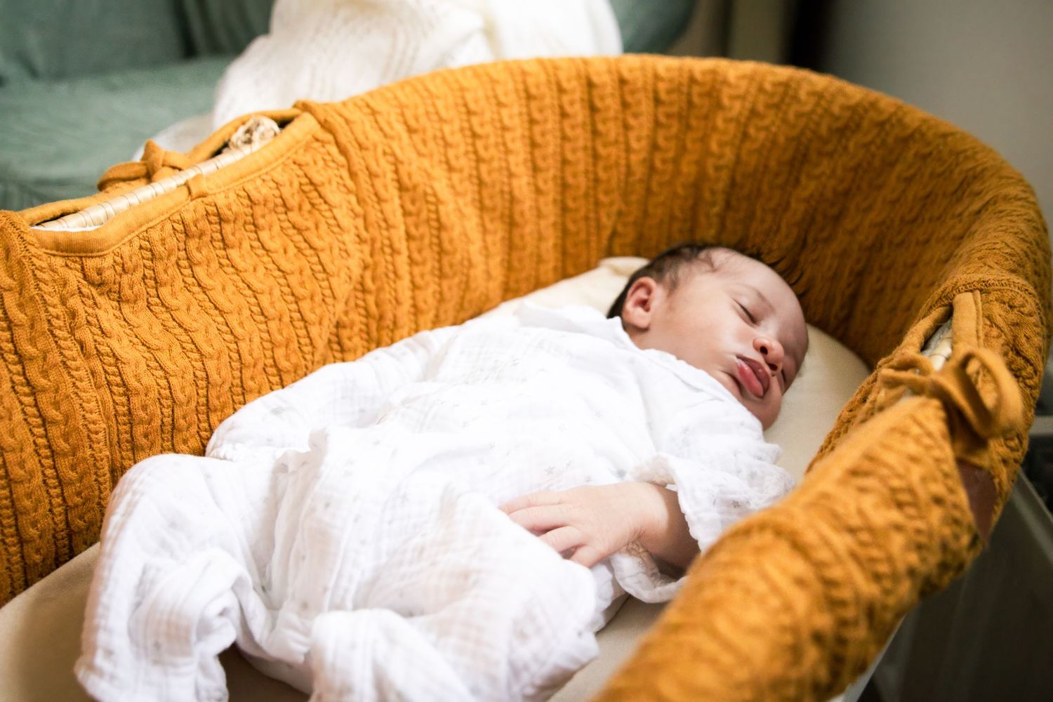 Baby sleeping peacefully on orange knit blanket in soft lighting.