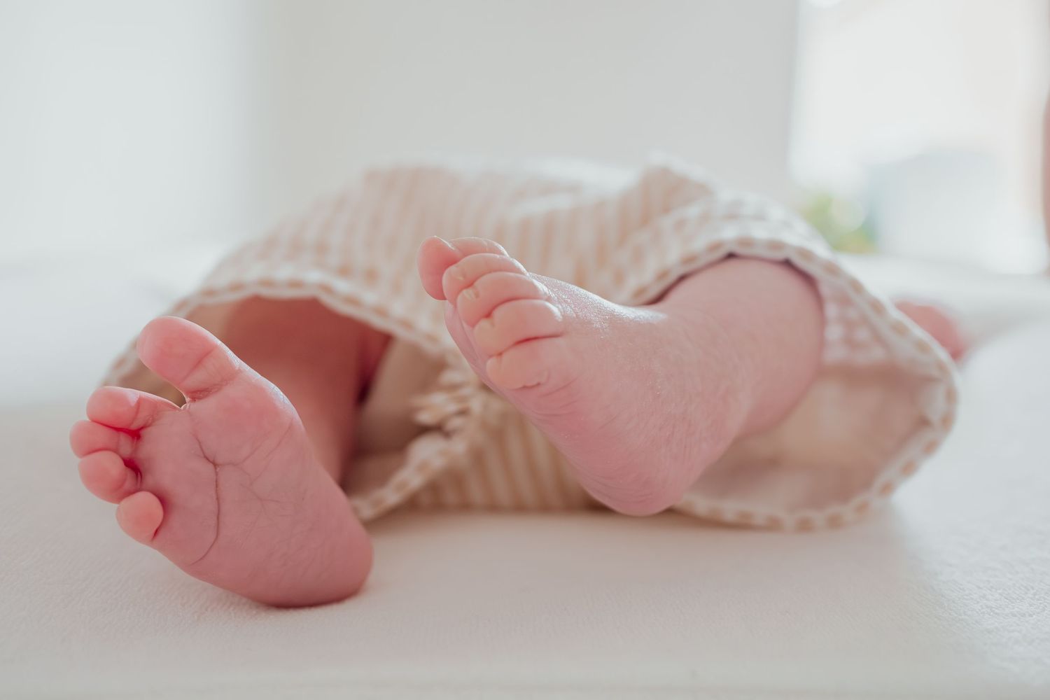 Close-up of adorable newborn baby feet peeking out from a soft striped blanket on a white surface.
