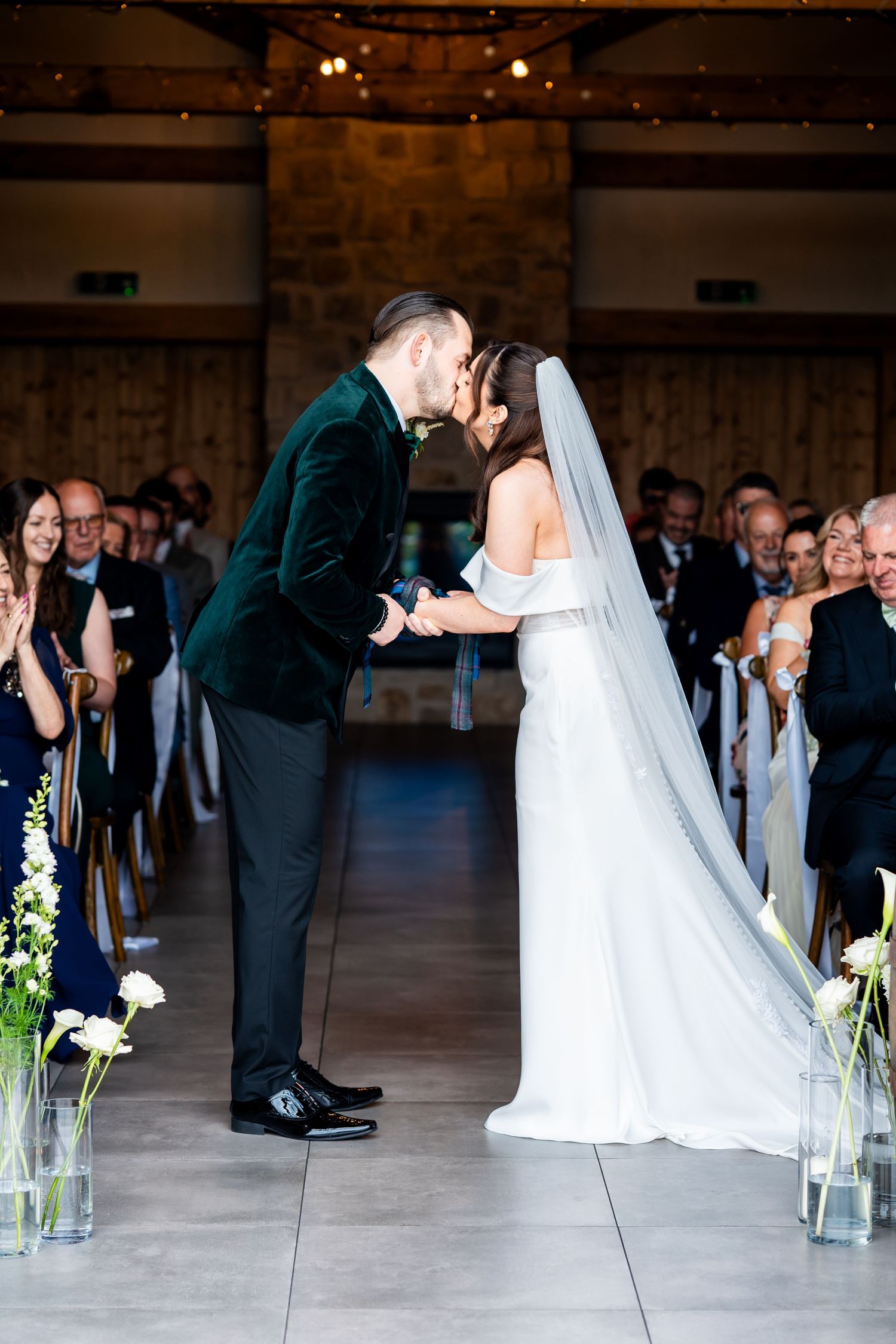 Bride and groom share their first kiss at the altar during a wedding ceremony in an elegant stone venue.