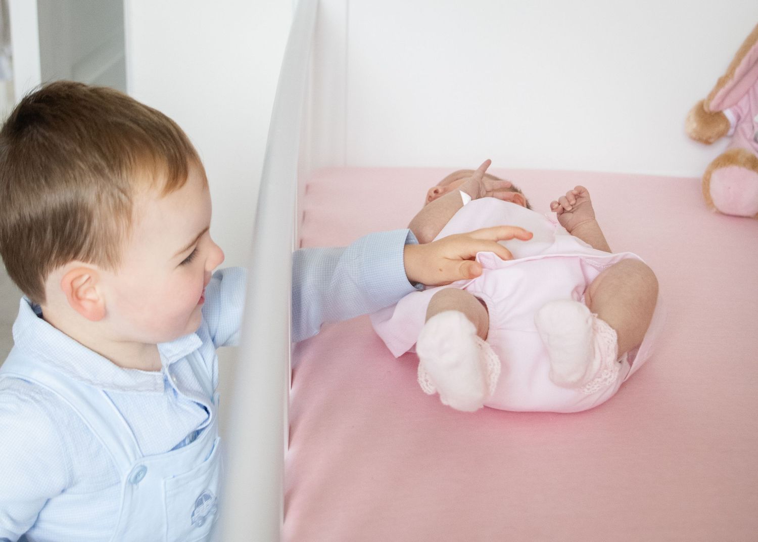 Baby in light blue outfit lying on pink bedding during lifestyle photoshoot.