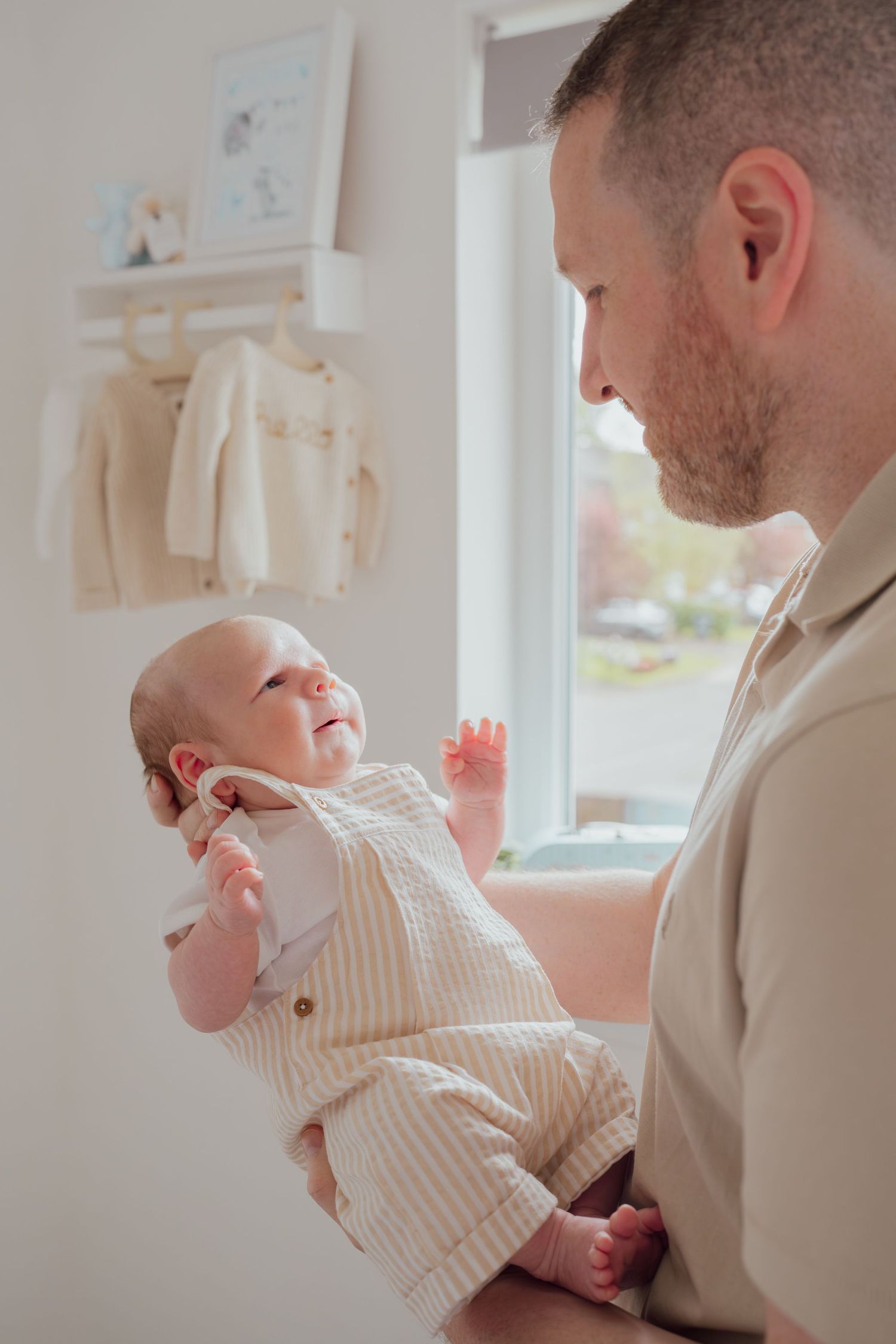 A bearded father lovingly holds his smiling newborn baby in a bright nursery room.