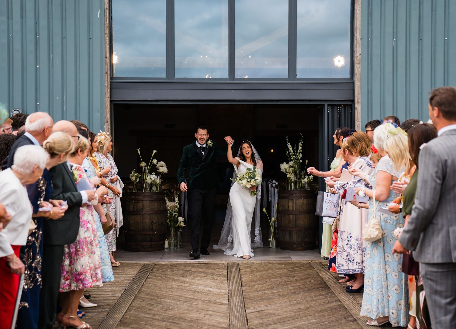 Newlywed couple exits barn wedding venue as guests celebrate with sparklers lining the aisle.