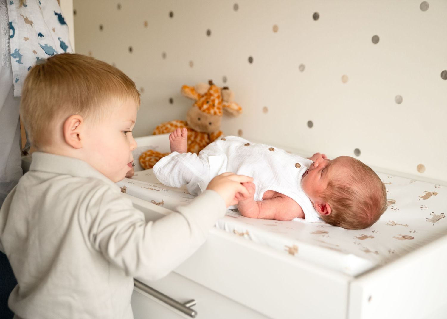 Series showing siblings meeting their new baby in a nursery with polka dot wallpaper.