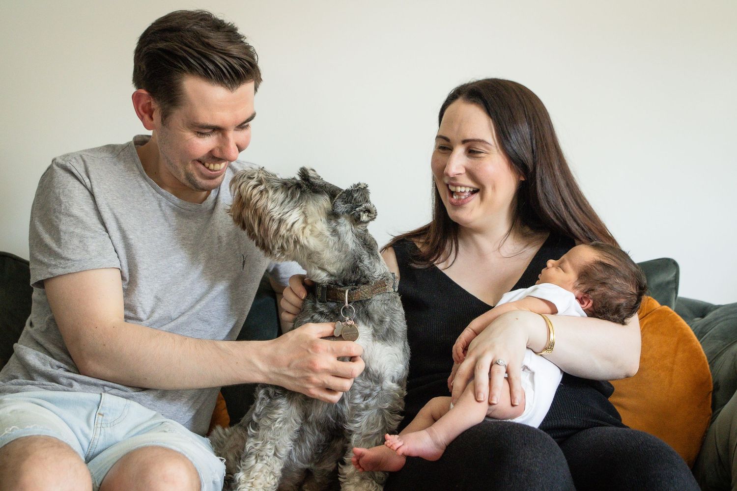 A family relaxing on a couch with their pet dog and baby.