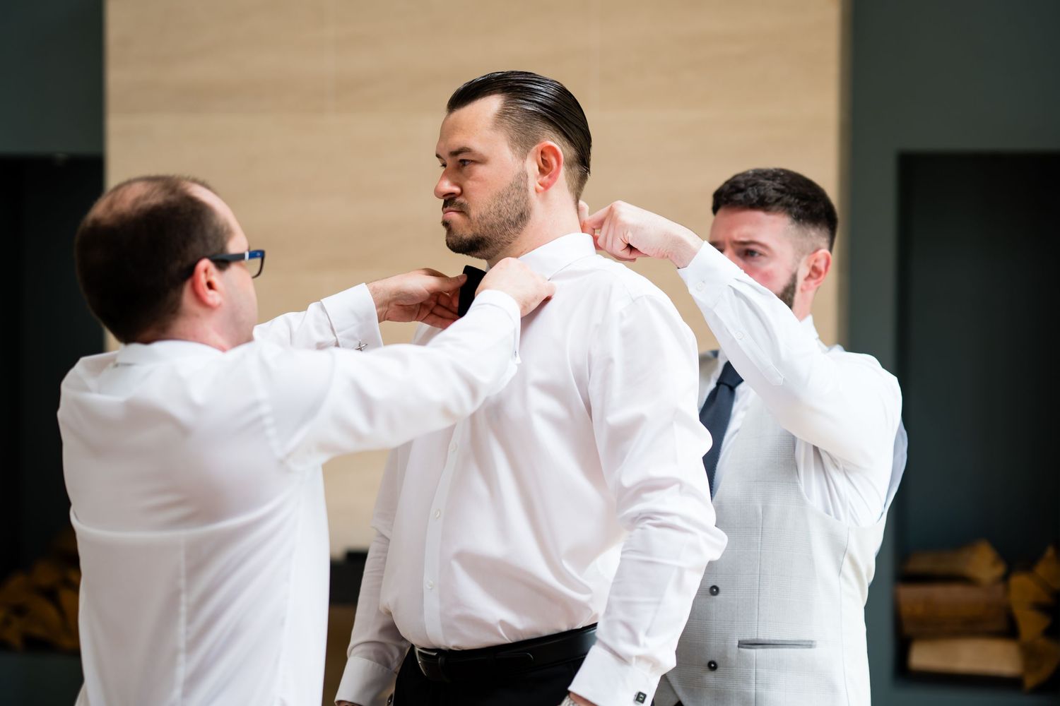 Groomsmen helping groom adjust his tie and collar while getting ready for wedding ceremony.