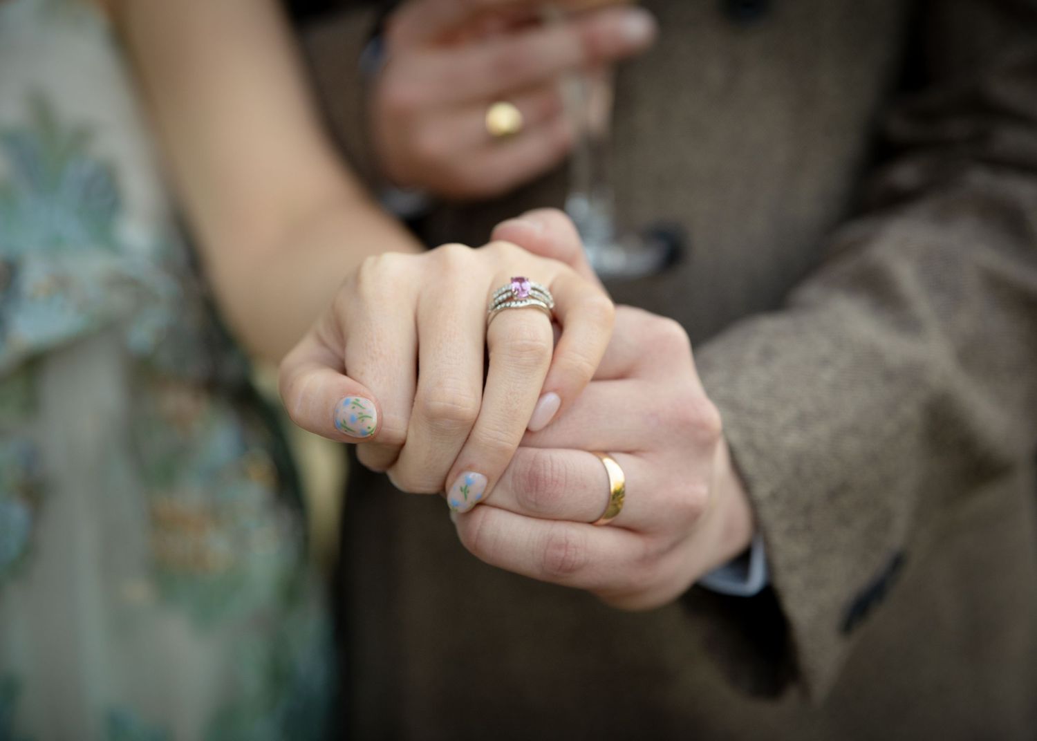 Close-up of hands showing wedding rings against a floral dress and suit.