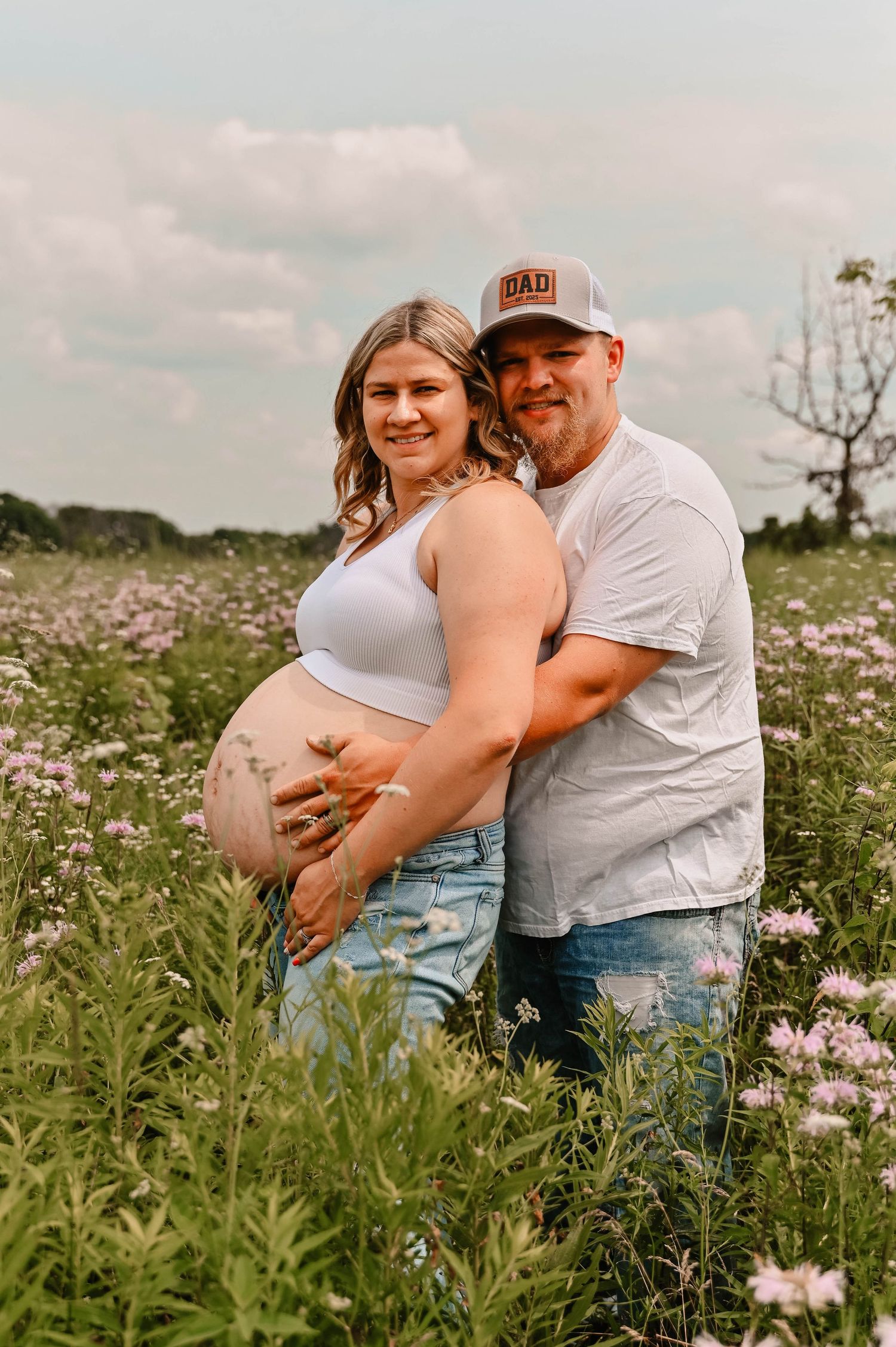A couple poses in a flowering meadow during sunset for maternity photos.