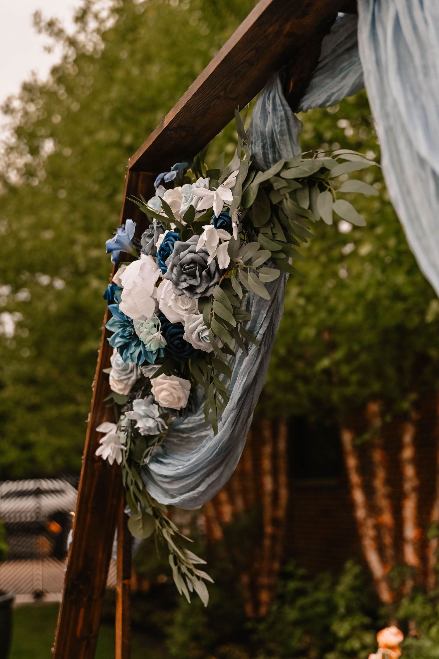 Wedding arch decorated with white roses and blue fabric draping against garden backdrop.