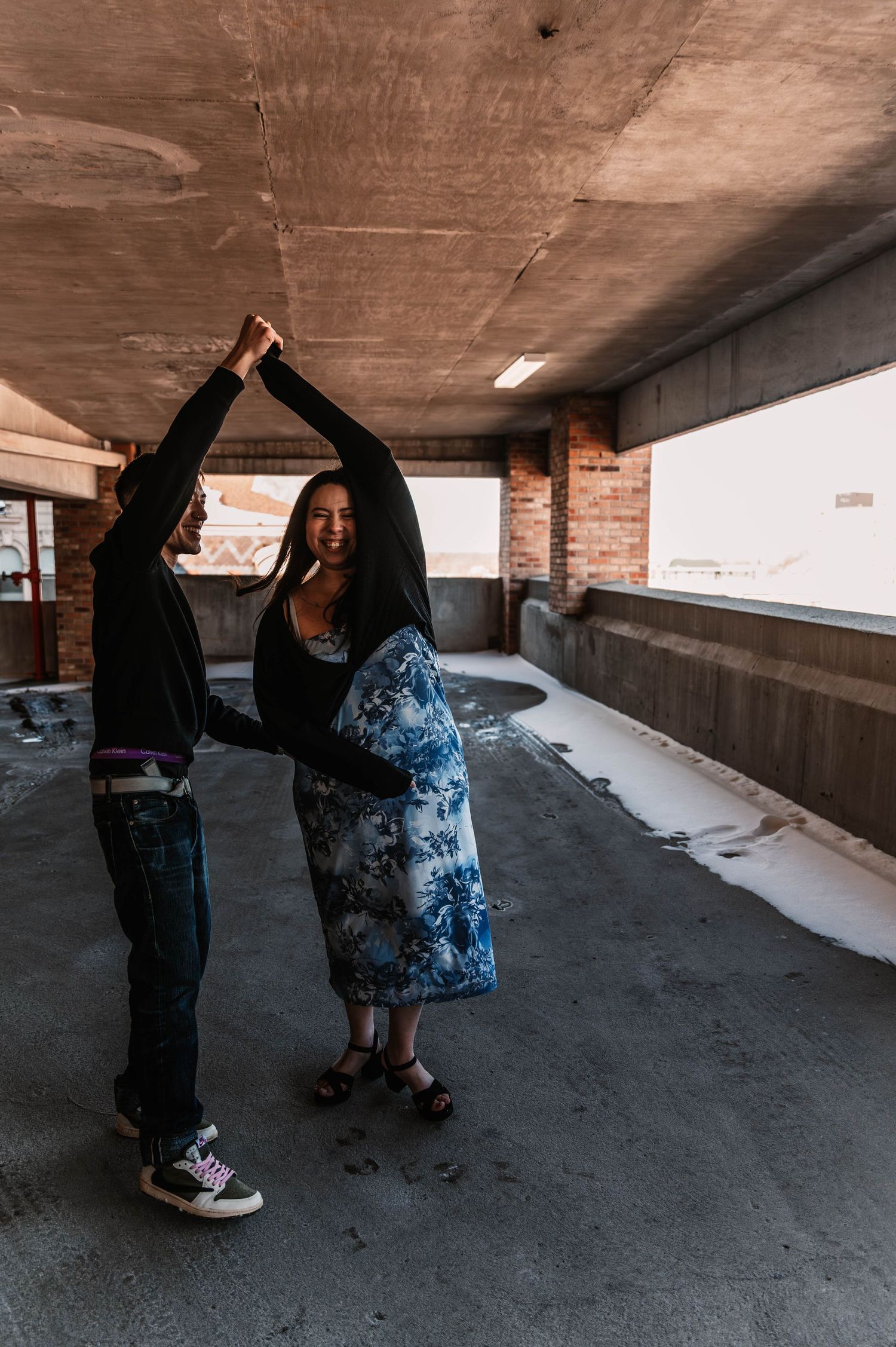 Two people in casual attire dance together in an urban concrete underpass setting.