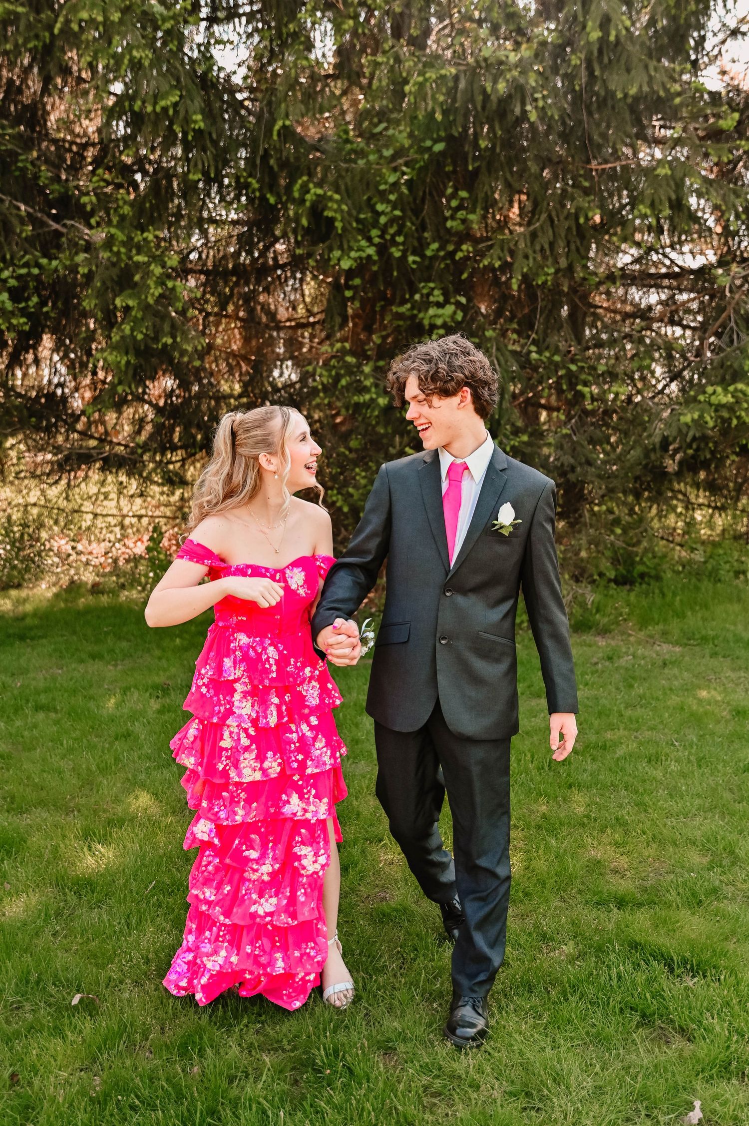 Couple in formal attire sharing playful moments on grass during photo session.