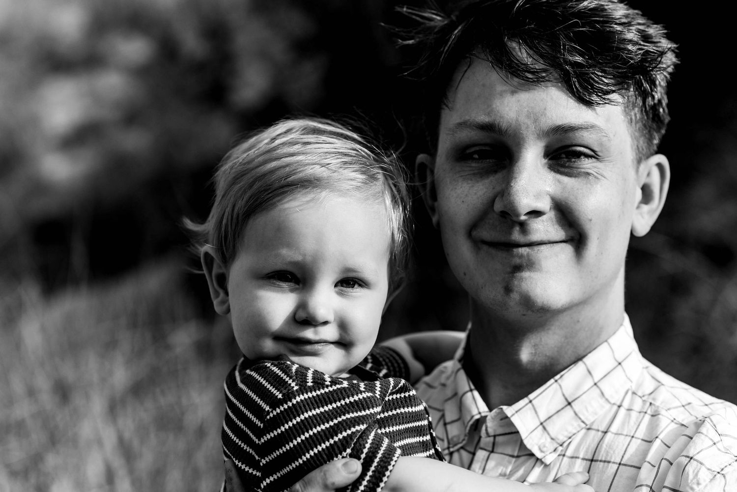 Black and white portrait of two people sharing a close moment outdoors.