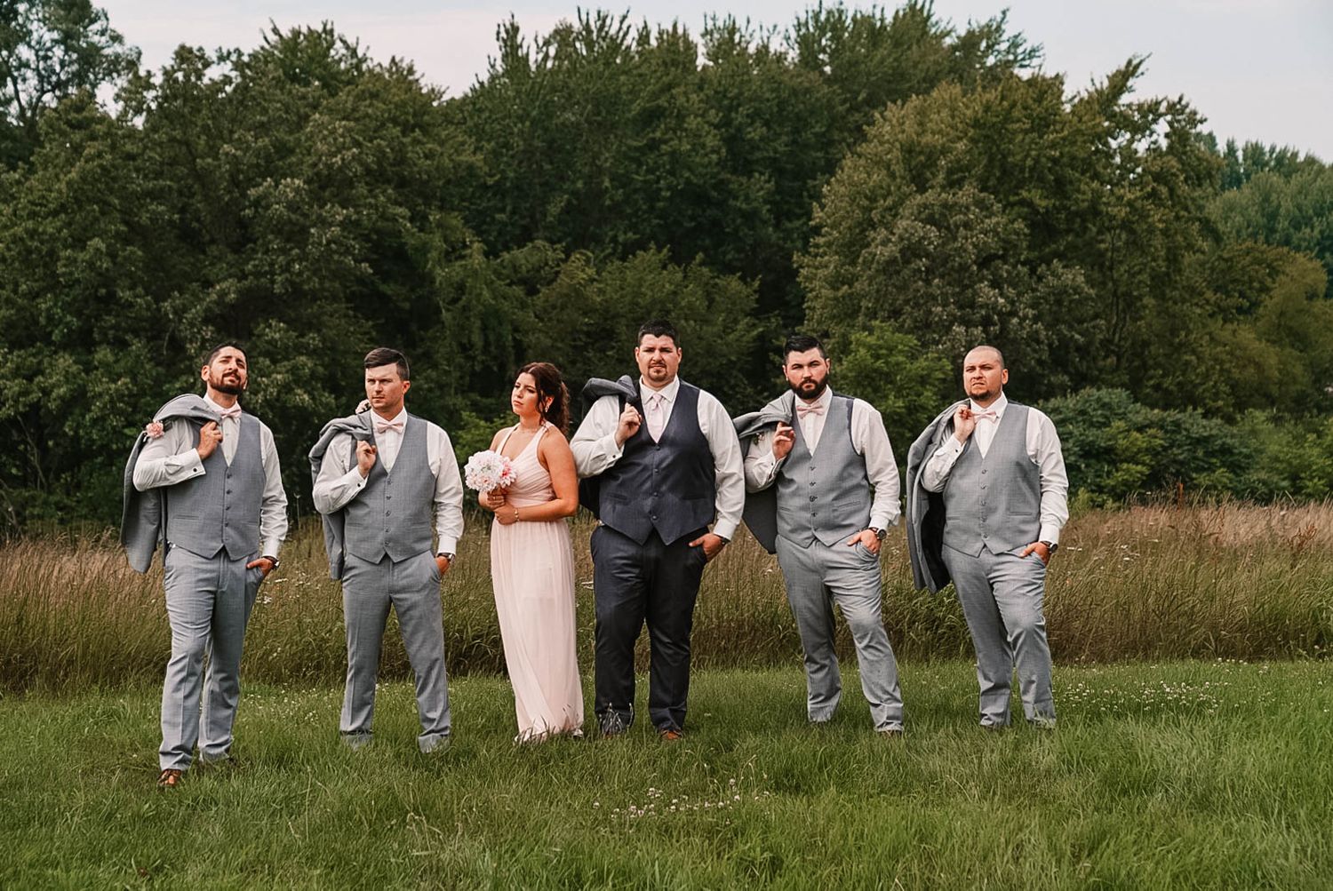 Wedding party poses casually in a grassy field wearing gray suits.