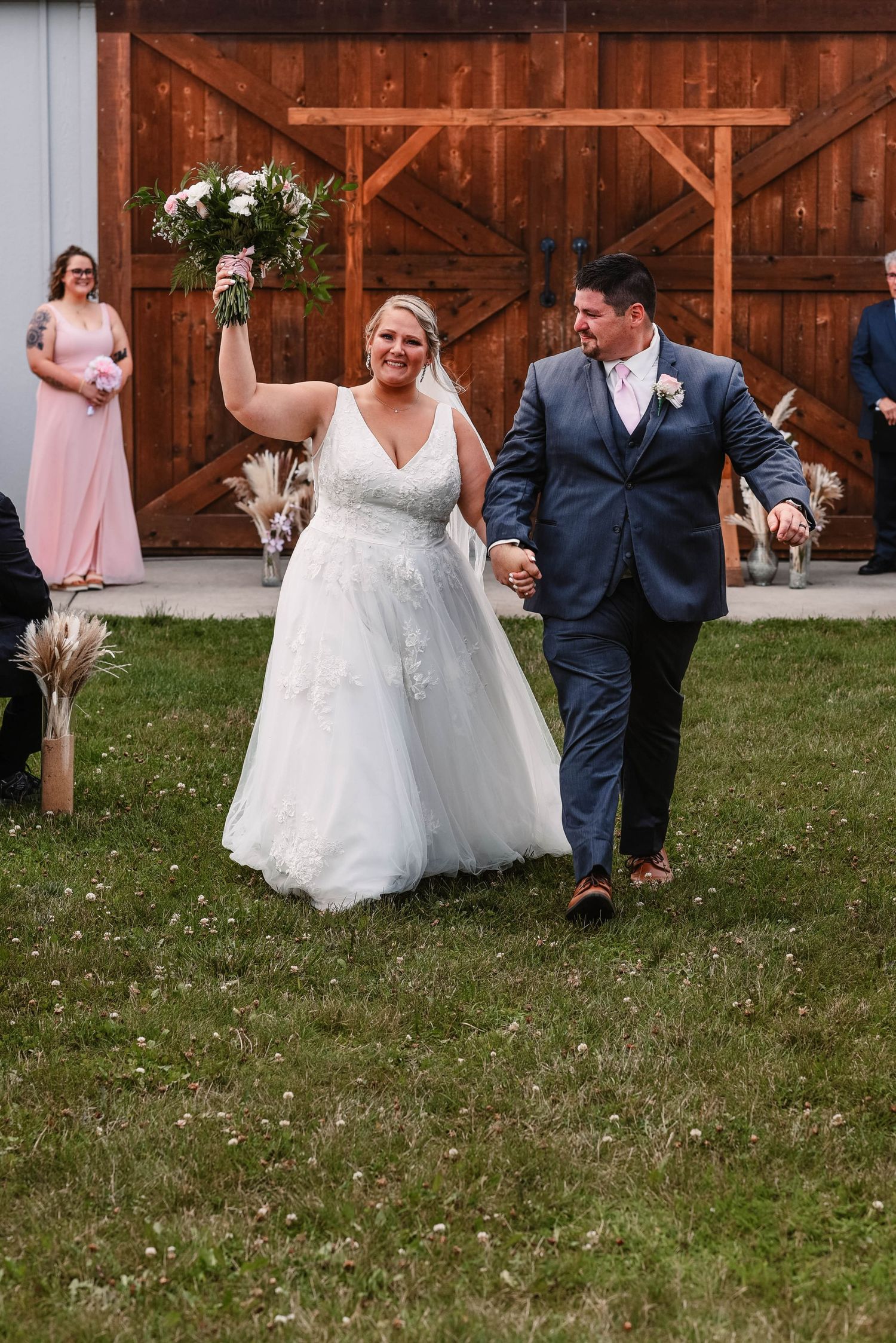 Wedding couple dances playfully on grass near a rustic barn venue.