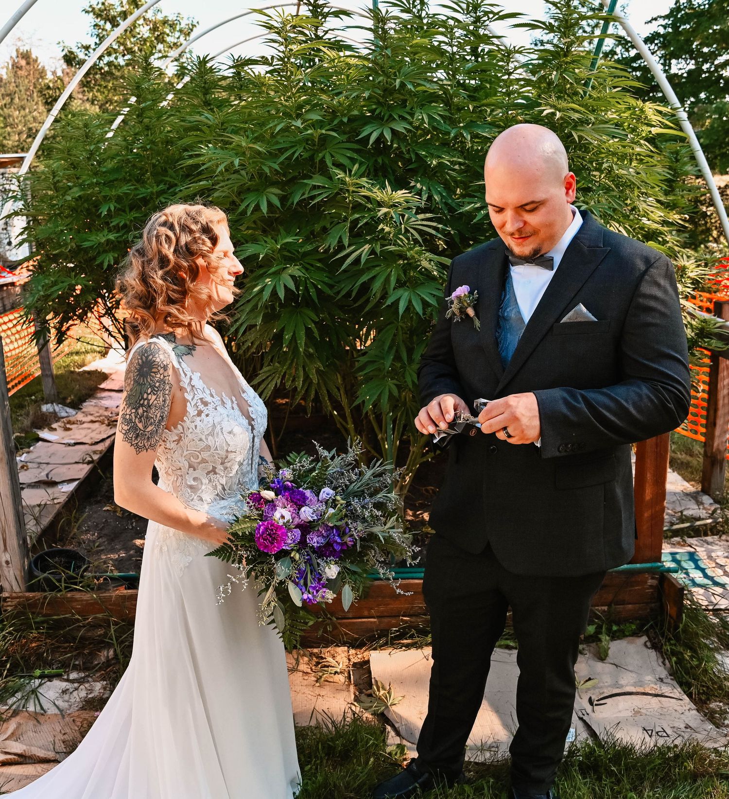 Couple sharing a moment under an outdoor arch with greenery and purple flowers.