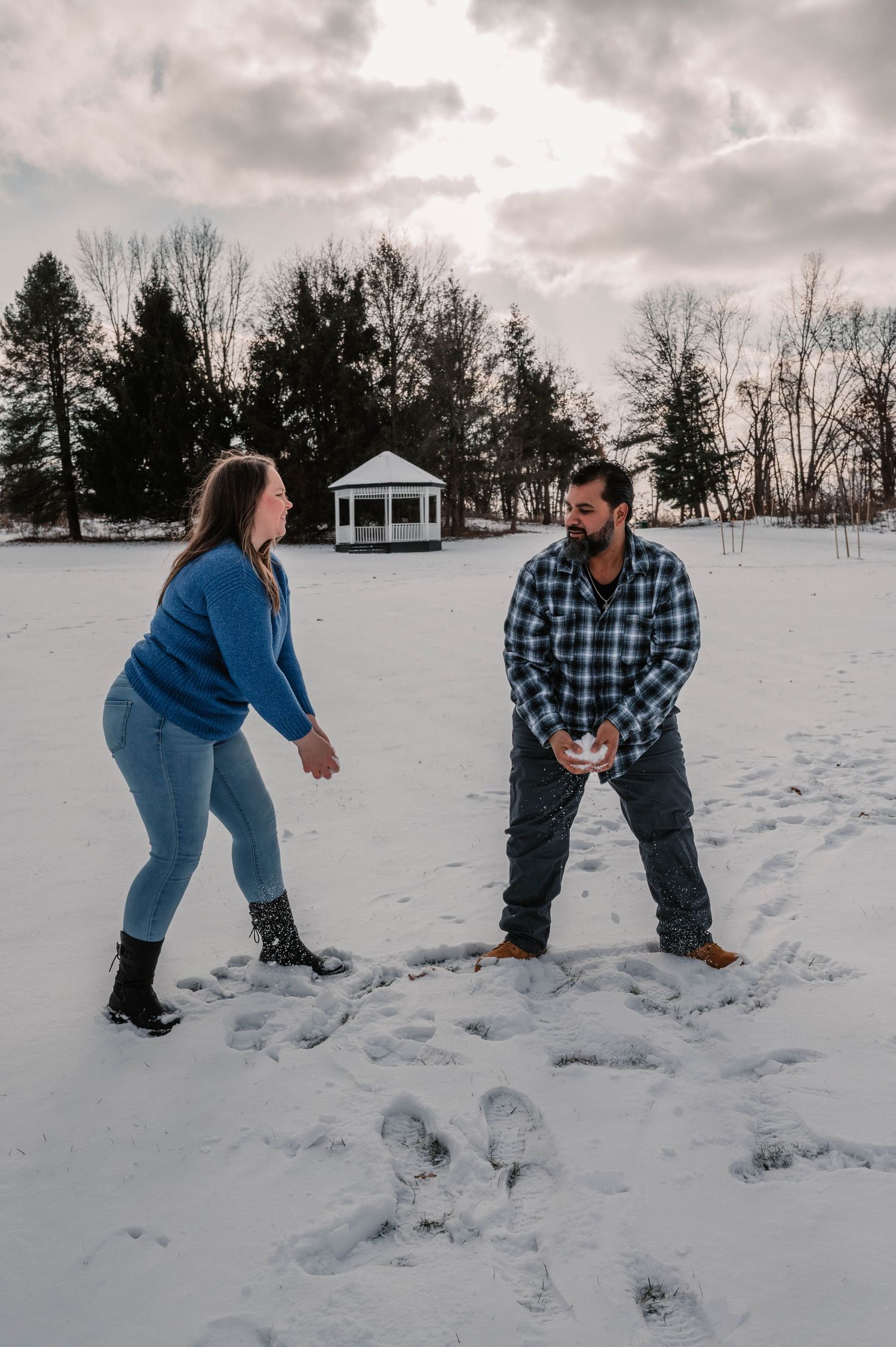 Two people having fun making snow angels in a snowy winter field with a gazebo in background.