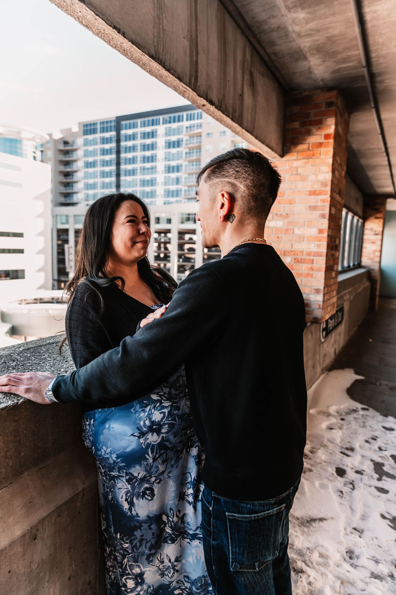 Couple embracing in a brick corridor with modern buildings in background.
