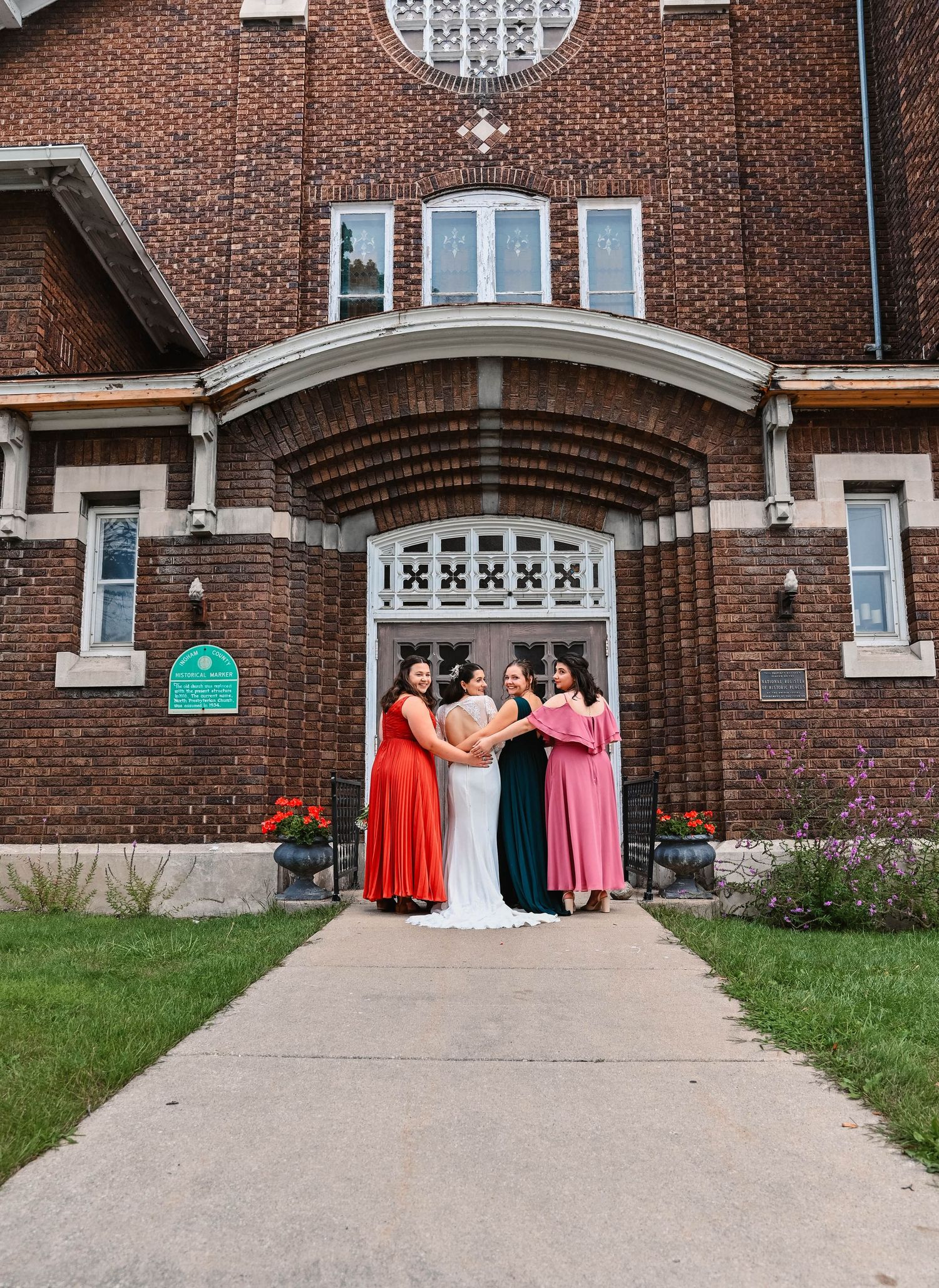 Wedding party in vibrant dresses standing under arched brick church entrance.